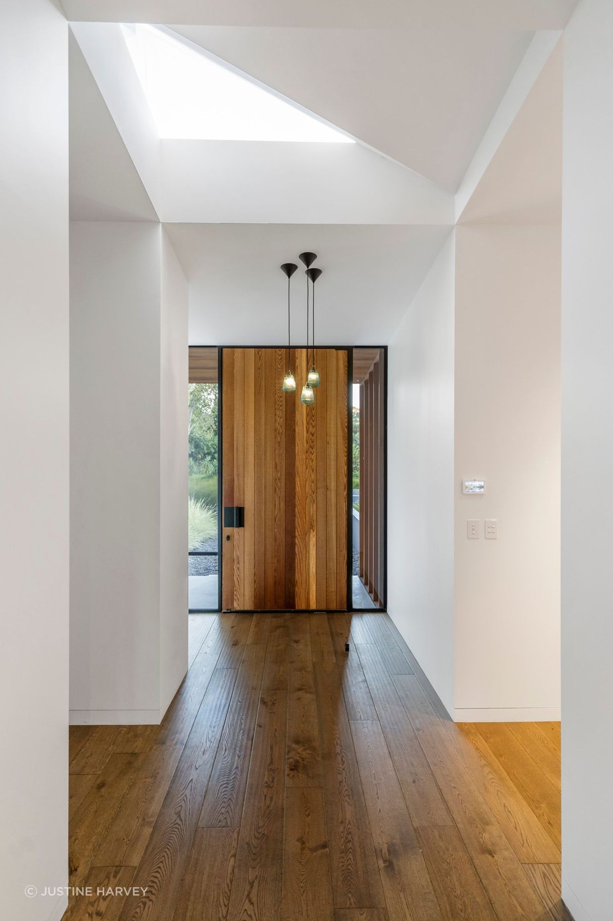 A cedar front door and dark oak flooring are top-lit by a triangular skylight.