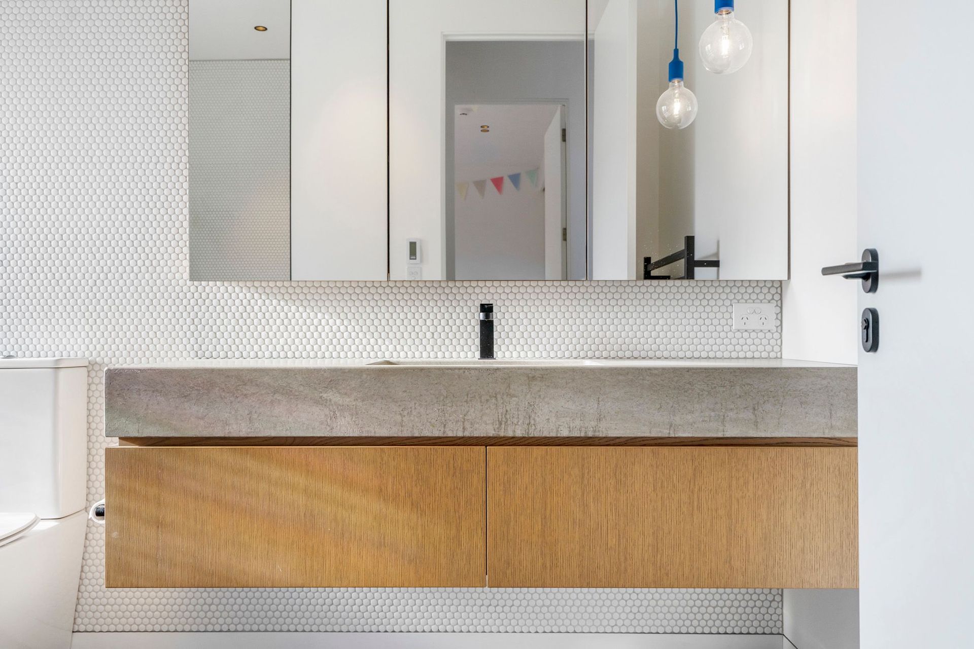 A concrete and oak vanity floats off the white tiled walls in the family bathroom.