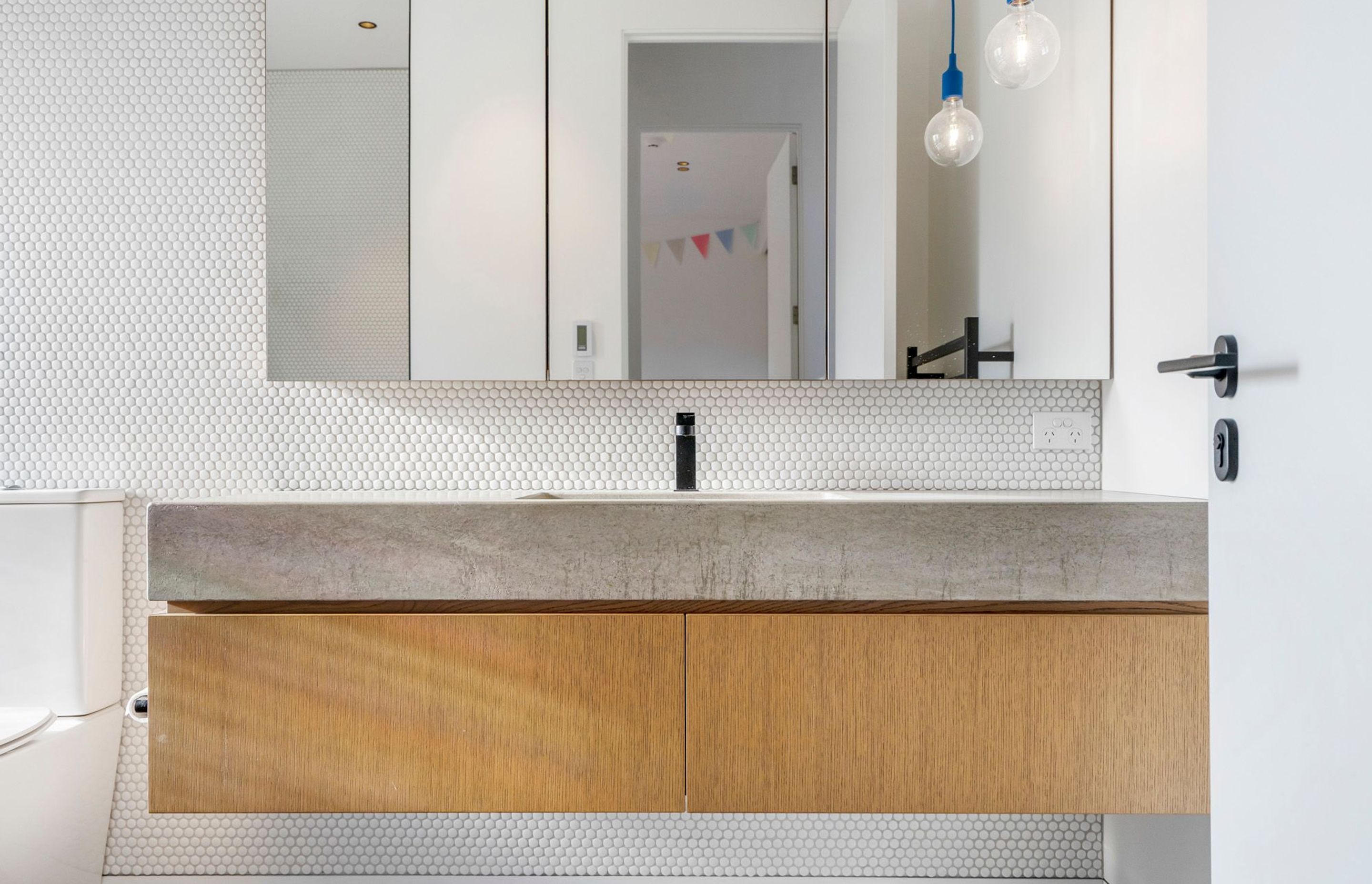 A concrete and oak vanity floats off the white tiled walls in the family bathroom.