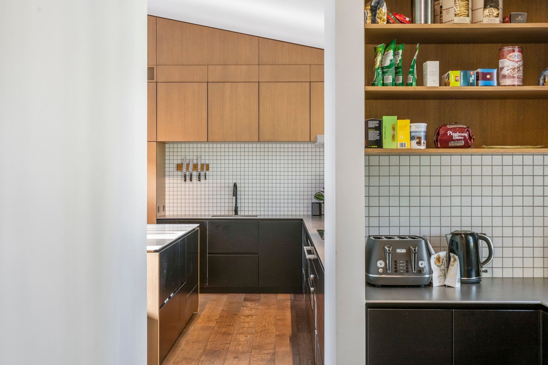 The adjacent scullery is hidden from the main kitchen and living area but is only a few paces away. White tiling with black grout and satin-finished steel worktops contrast the black and timber cabinetry.