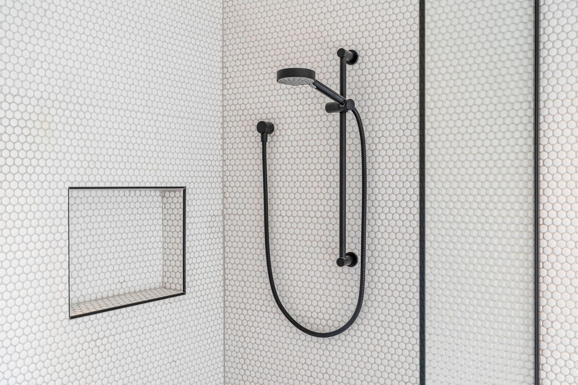 This monochromatic shower in the family bathroom contrasts modern black tapware against the small circular tiles.