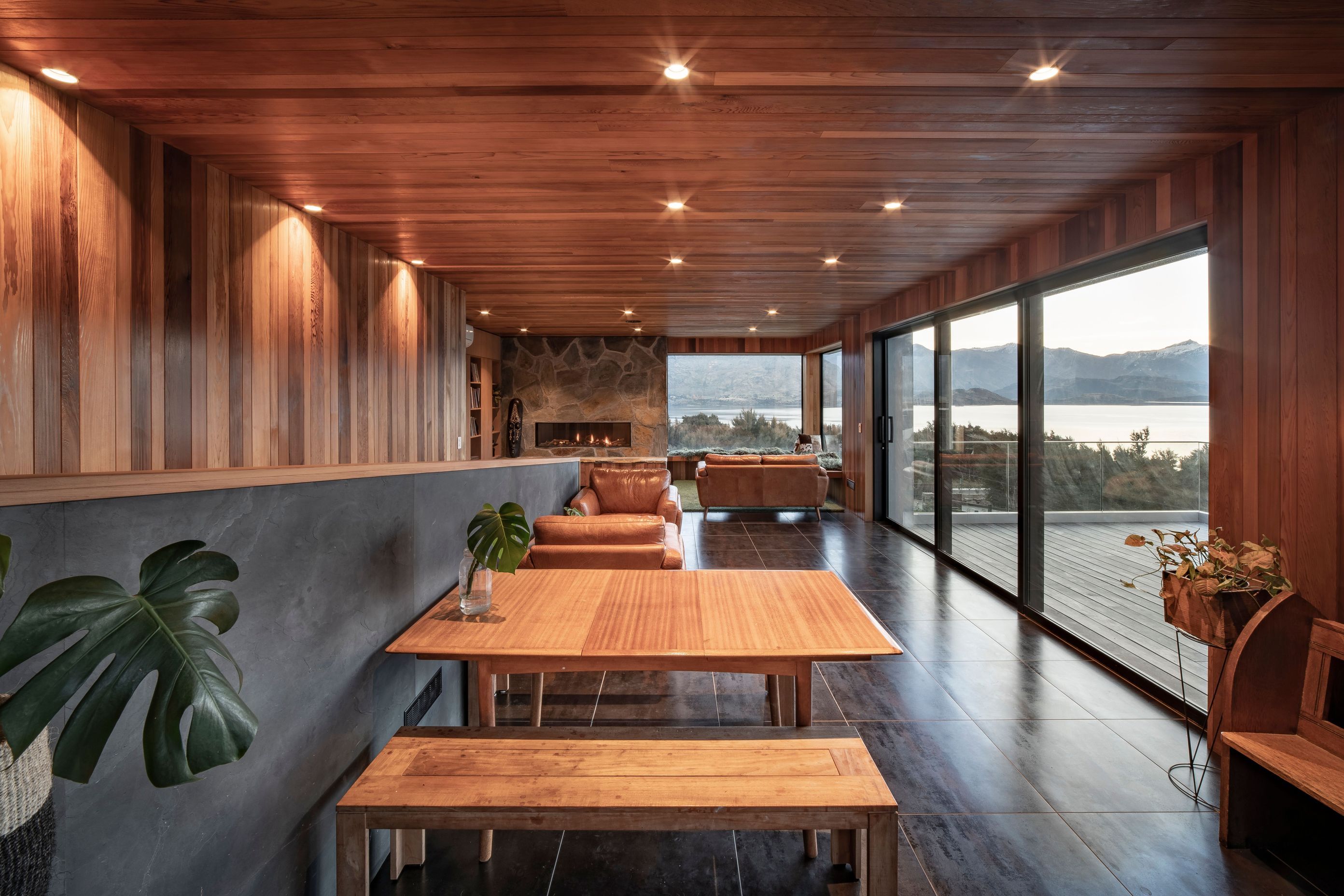 The open-plan dining and living area opens out to the deck on the right. A staircase on the left leads to the lower-level gallery/hallway.