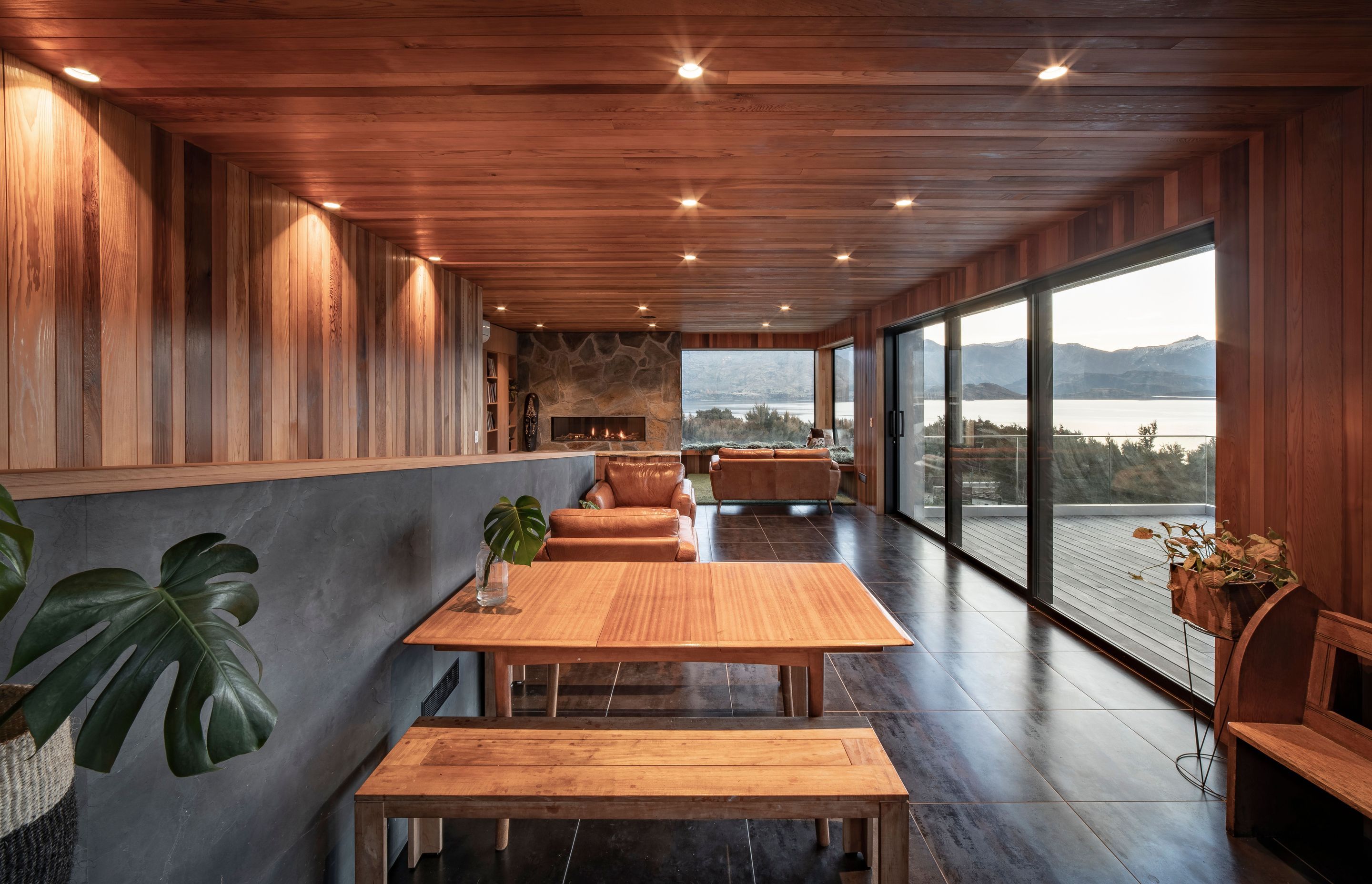 The open-plan dining and living area opens out to the deck on the right. A staircase on the left leads to the lower-level gallery/hallway.