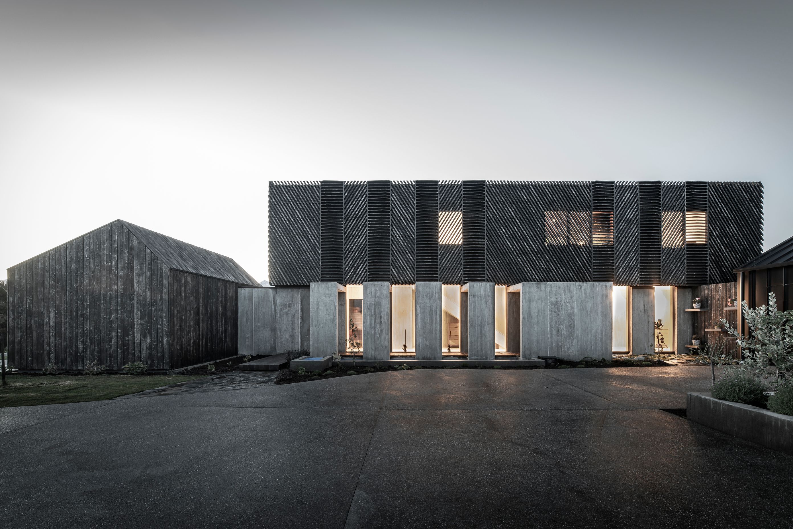 The southern elevation lit up at dusk highlights the screening over the windows and the glazing into the internal gallery/hallway.