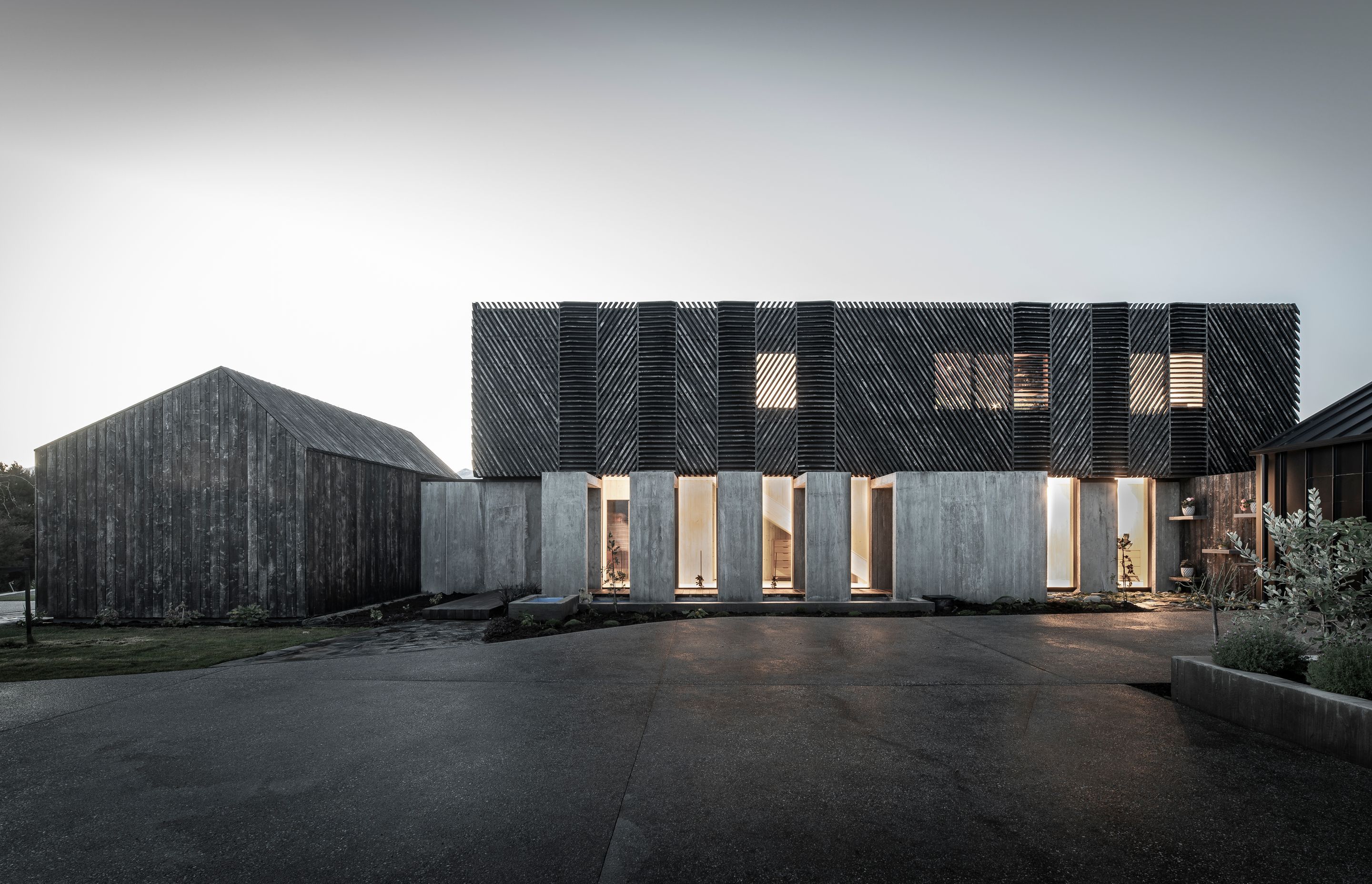 The southern elevation lit up at dusk highlights the screening over the windows and the glazing into the internal gallery/hallway.