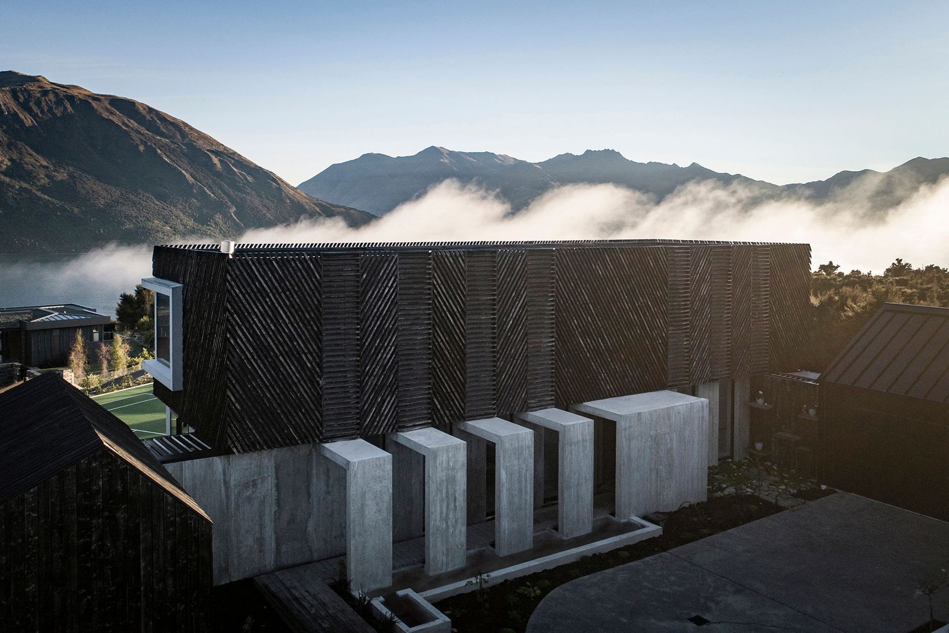 Low-lying cloud over the lake creates a dramatic backdrop to Mount Gold house. In the foreground, the exterior concrete corridor forms a procession to the entry of the house.