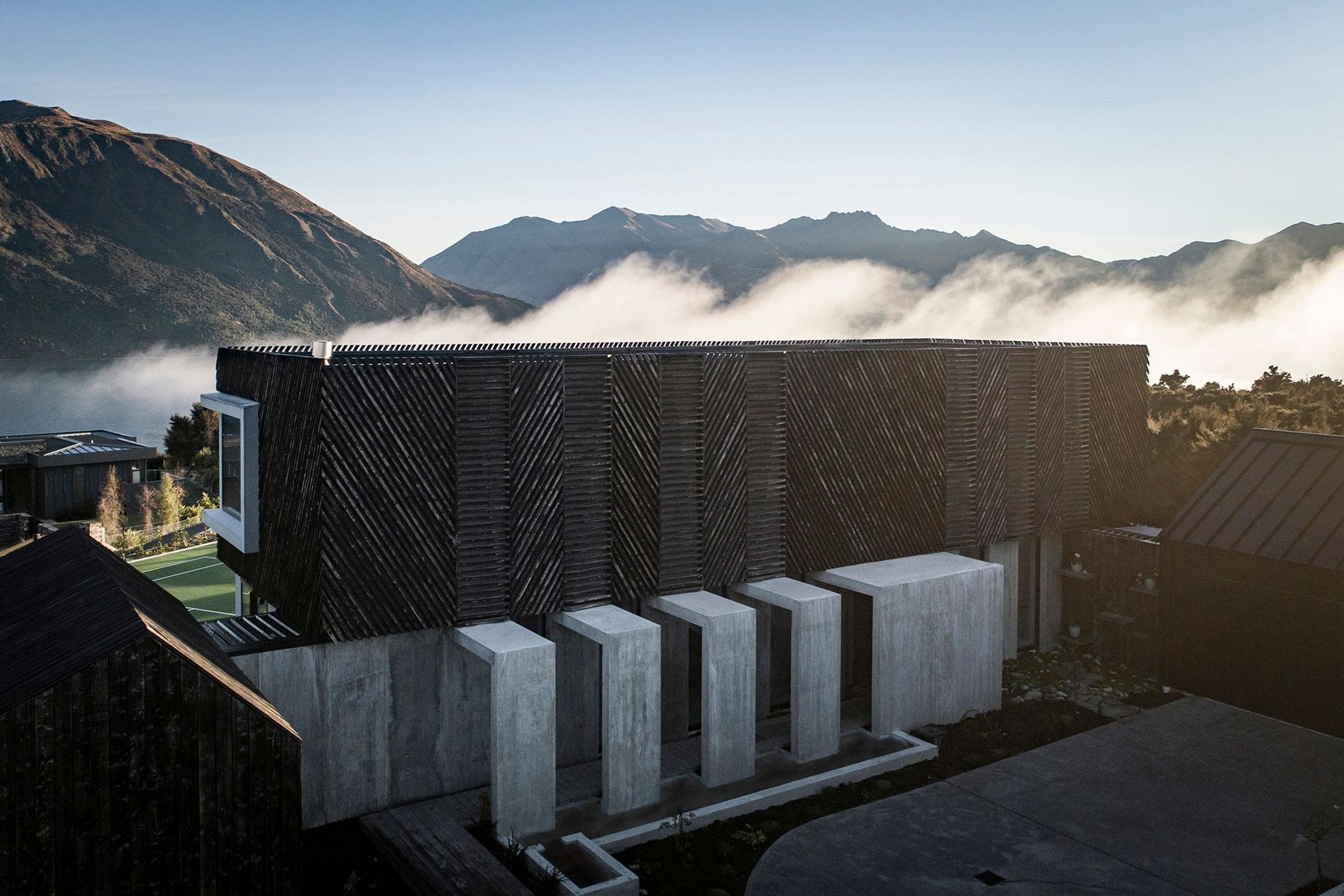 Low-lying cloud over the lake creates a dramatic backdrop to Mount Gold house. In the foreground, the exterior concrete corridor forms a procession to the entry of the house.
