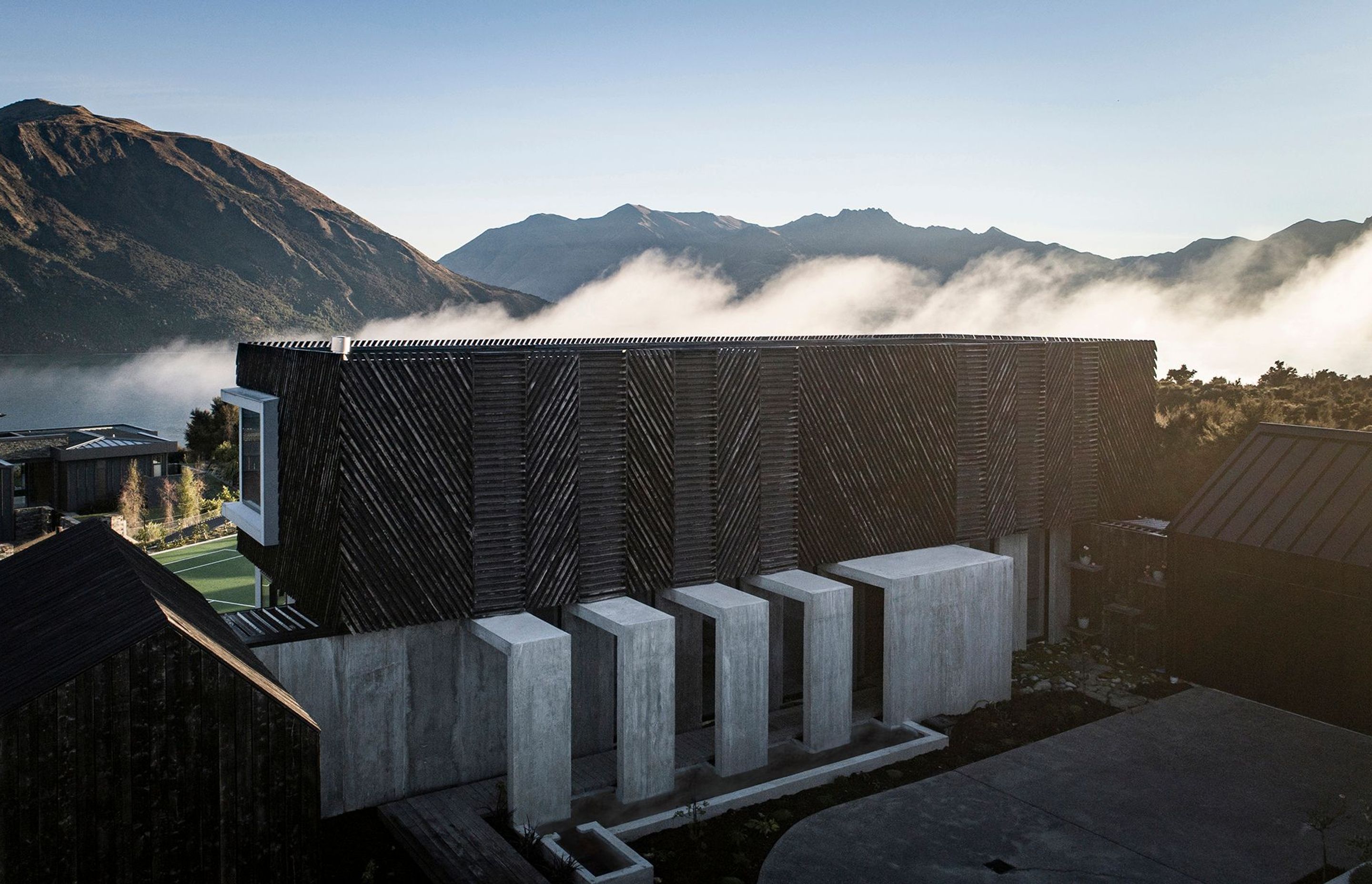 Low-lying cloud over the lake creates a dramatic backdrop to Mount Gold house. In the foreground, the exterior concrete corridor forms a procession to the entry of the house.