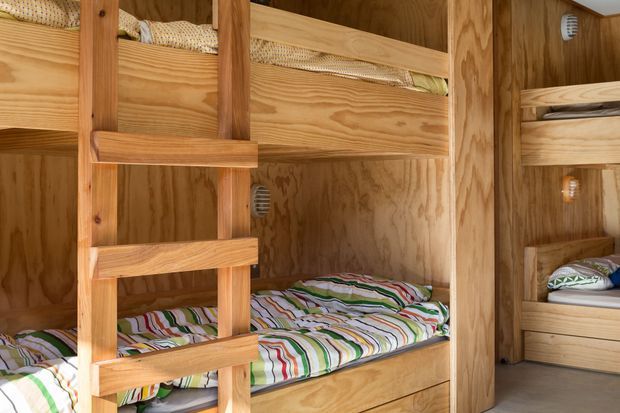 Compact bunk-bed sleeping area built entirely with warm-toned timber, including built-in bunk frames, ladder, drawer storage, and plywood wall and ceiling finishes. Patterned striped bedding adds colour to the otherwise natural wood interior.