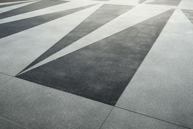 Close-up view of a geometric pavement or hardscape composed of alternating light and dark grey concrete or stone sections. Long triangular forms radiate across the surface, creating a bold monochromatic linear pattern.