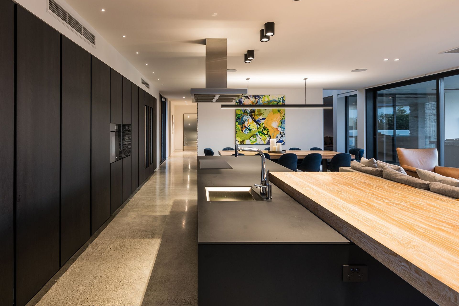 The Poliform kitchen features an expansive wall of cabinetry with built-in wine fridges and a long black island with a chunky timber breakfast bar.