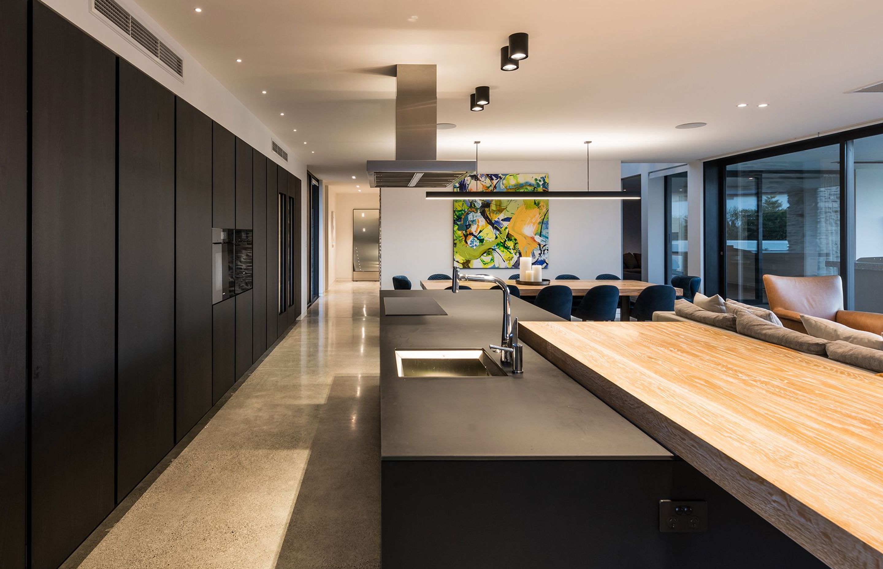 The Poliform kitchen features an expansive wall of cabinetry with built-in wine fridges and a long black island with a chunky timber breakfast bar.