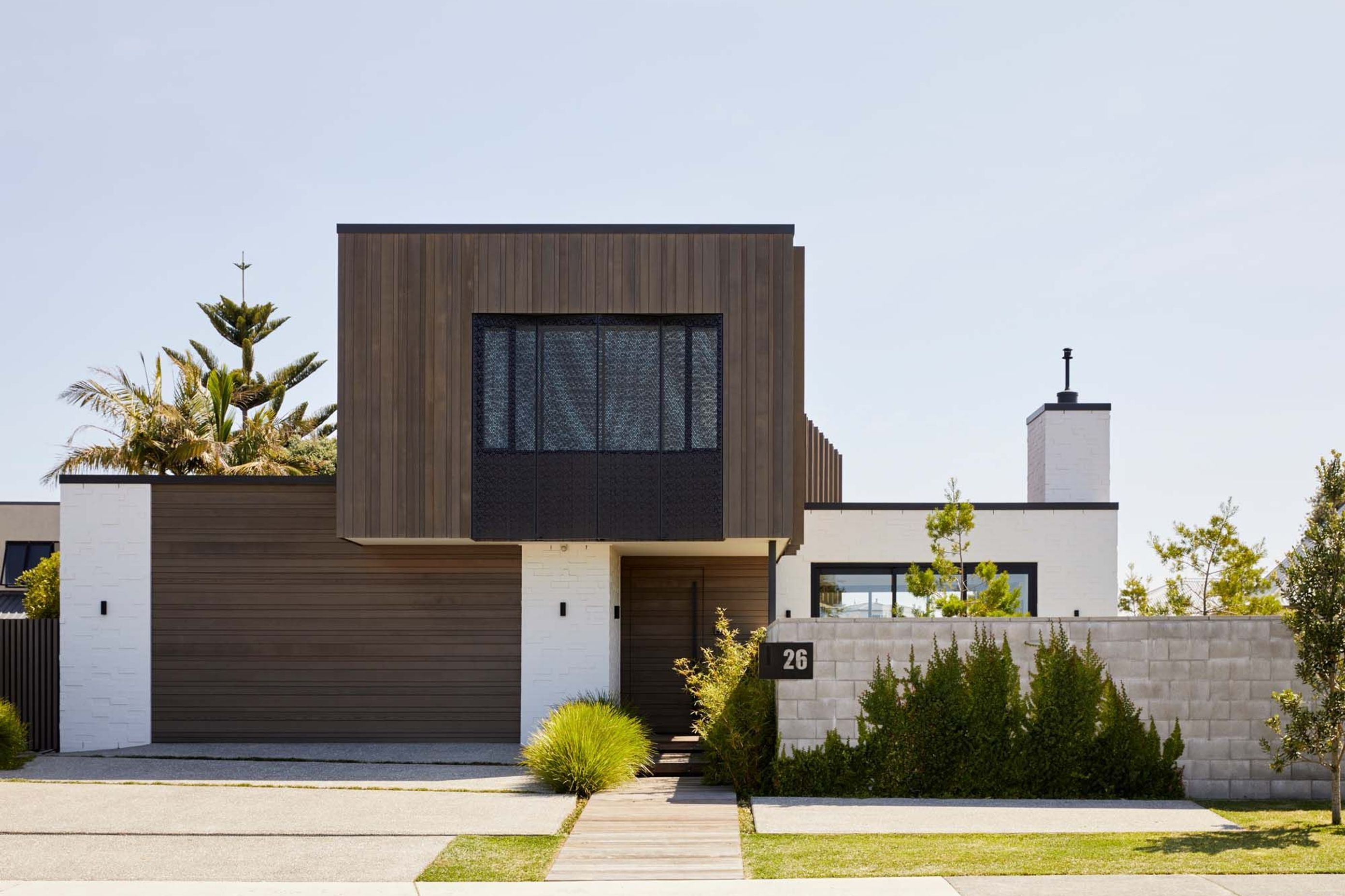The street elevation has garage and front doors recede into the building, with the upper floor poppiing out out, cantillevered over the front entry, while a blockwork boundary wall will form a green wall once the plants are established,