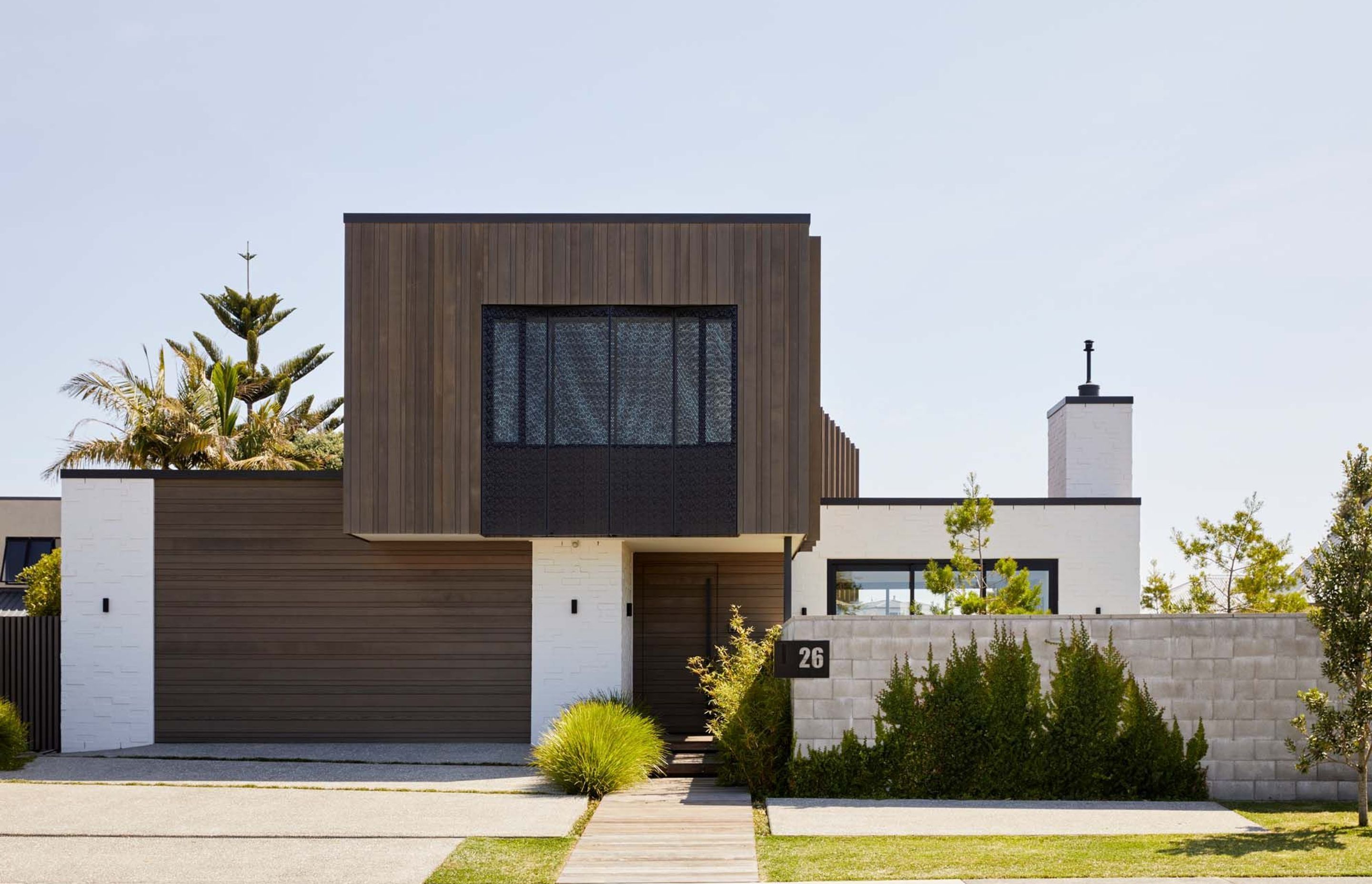 The street elevation has garage and front doors recede into the building, with the upper floor poppiing out out, cantillevered over the front entry, while a blockwork boundary wall will form a green wall once the plants are established,