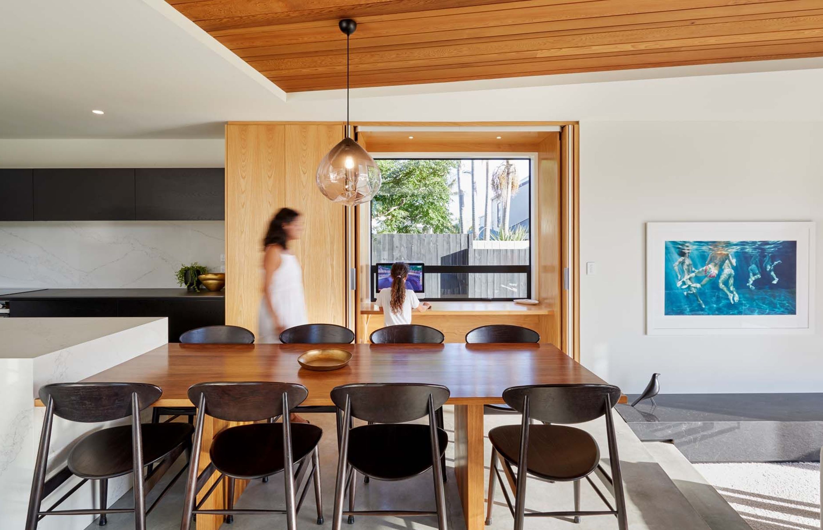 Timber furniture, cabinetry and ceiling adds warmth to the monochromatic colour scheme in the kitchen and dining area.