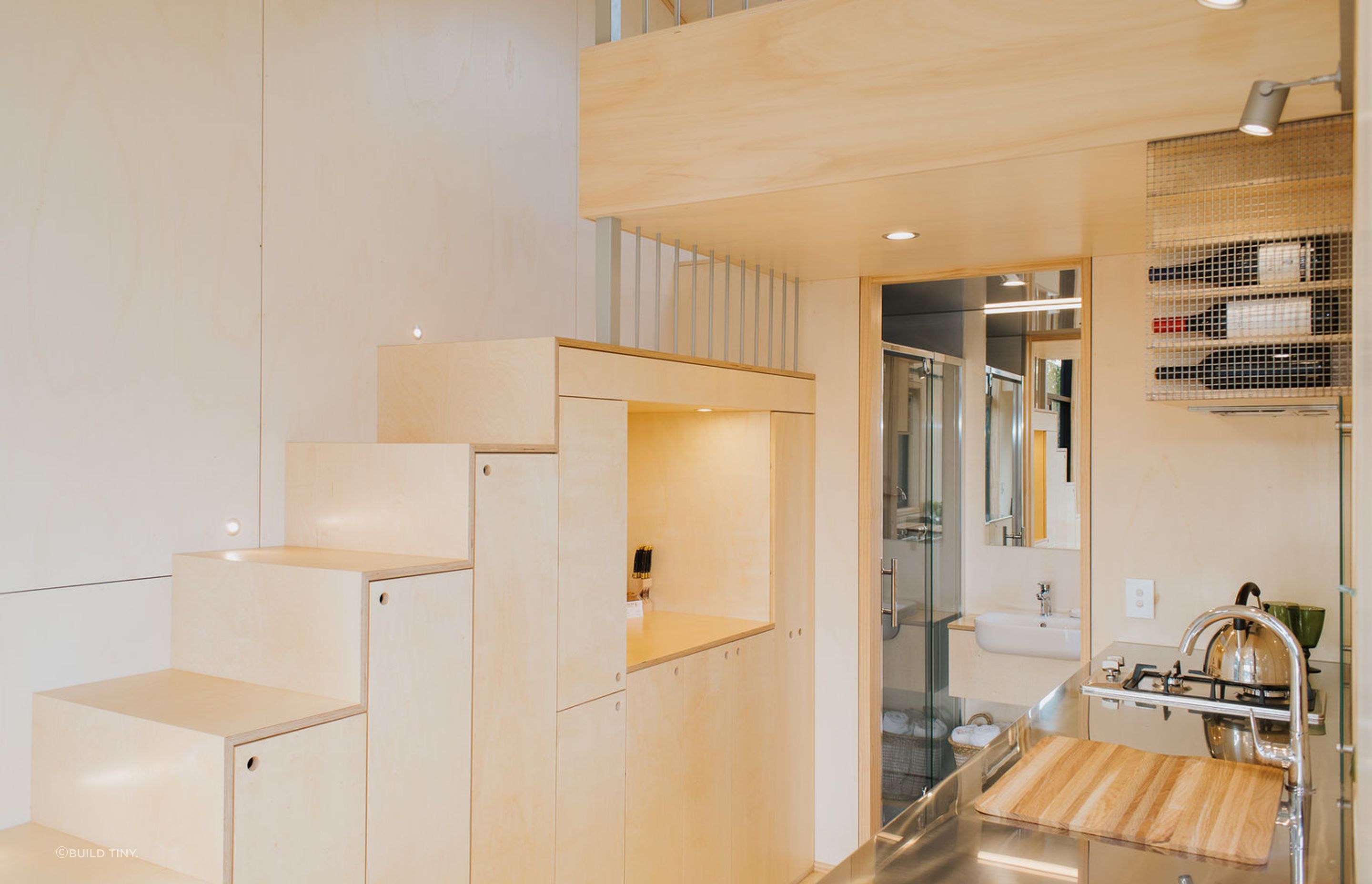 The plywood staircase incorporates cupboards and an alcove for kitchen and household storage. Photography supplied by Build Tiny.