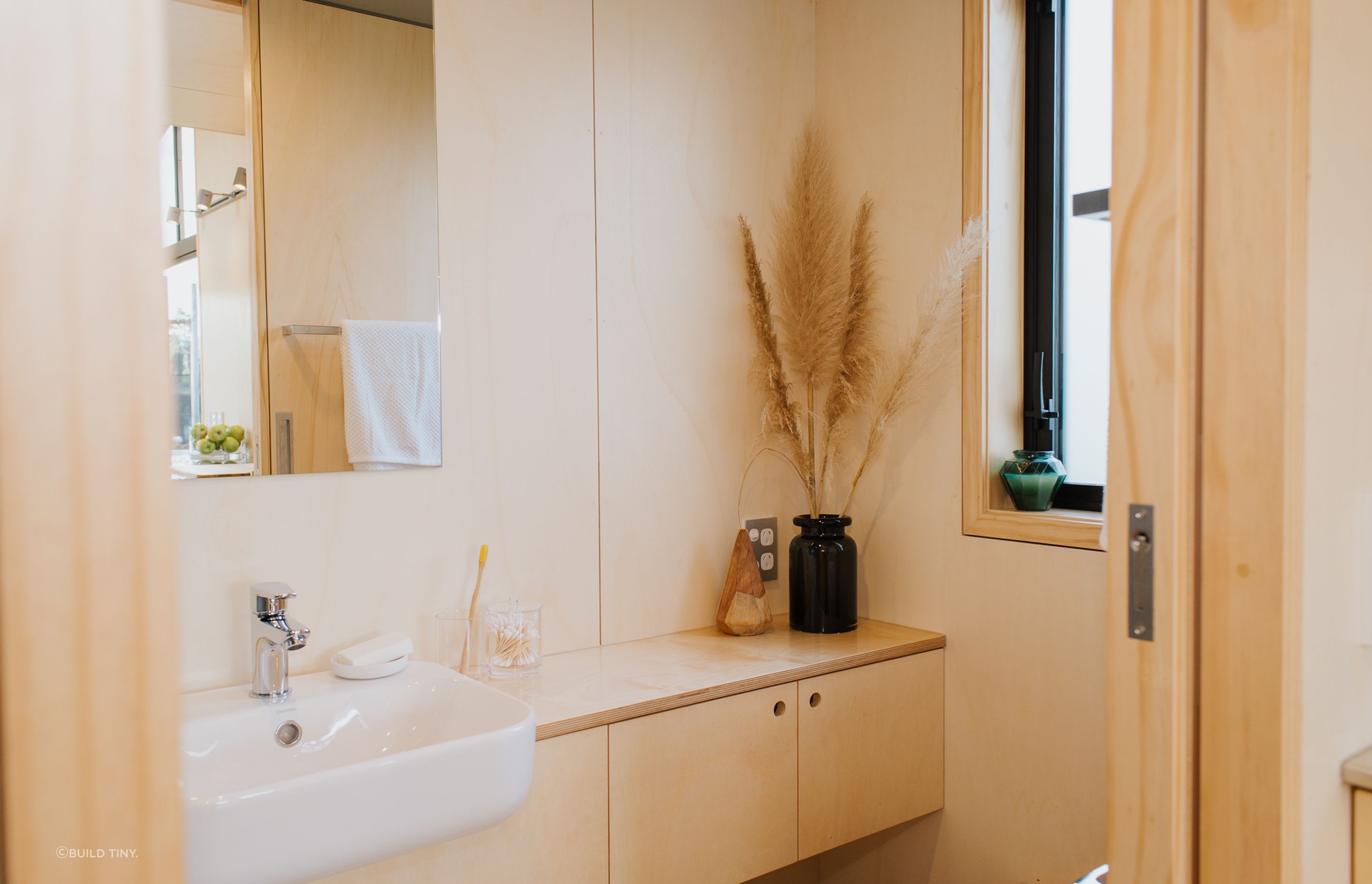 The bathroom features a cavilty sliding door, built-in plywood storage and a bamboo composting toilet. Photography supplied by Build Tiny.