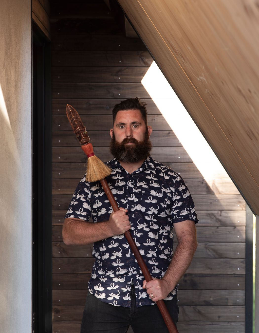 Designer Craig Wilson in the porch of his new home holding his taiaha.