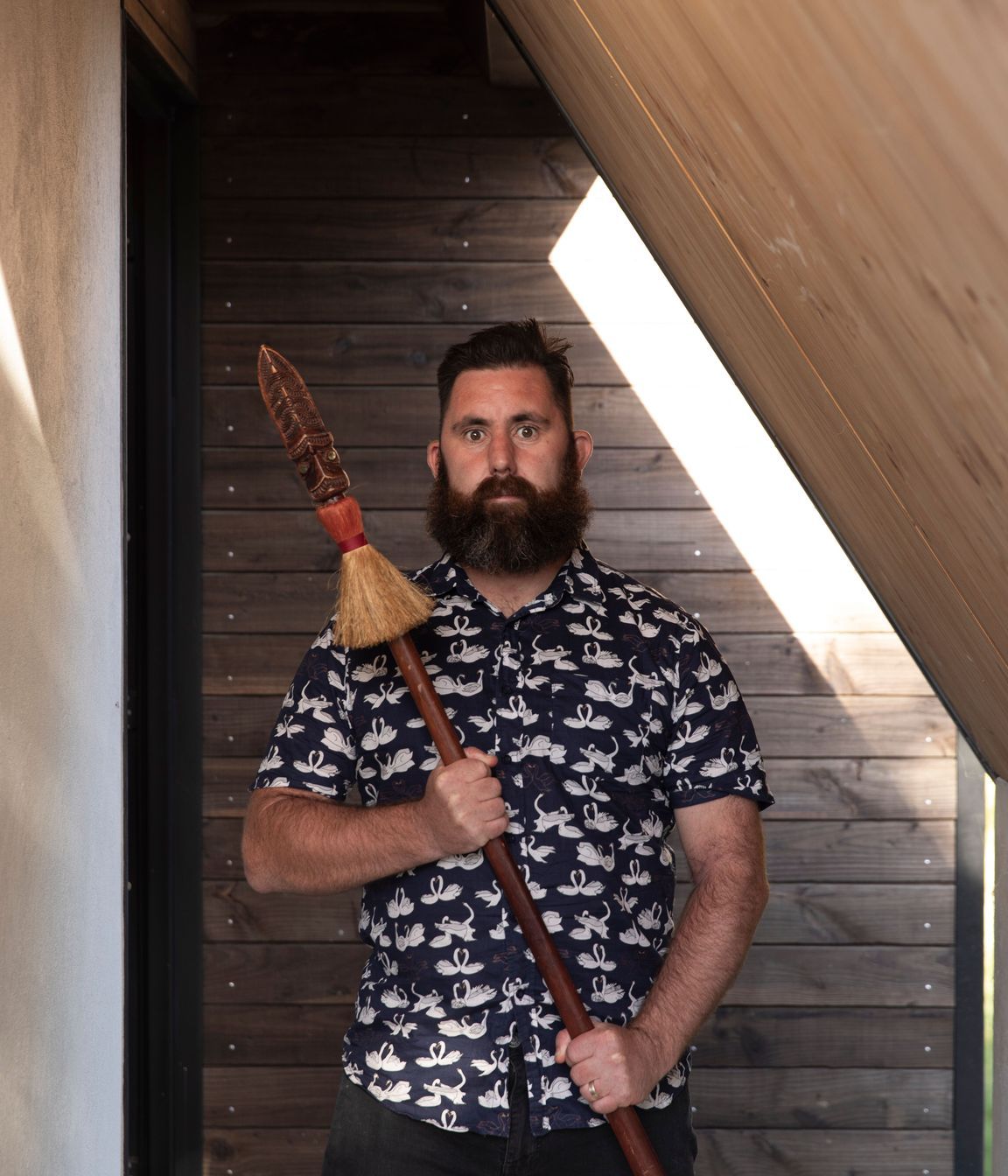 Designer Craig Wilson in the porch of his new home holding his taiaha.