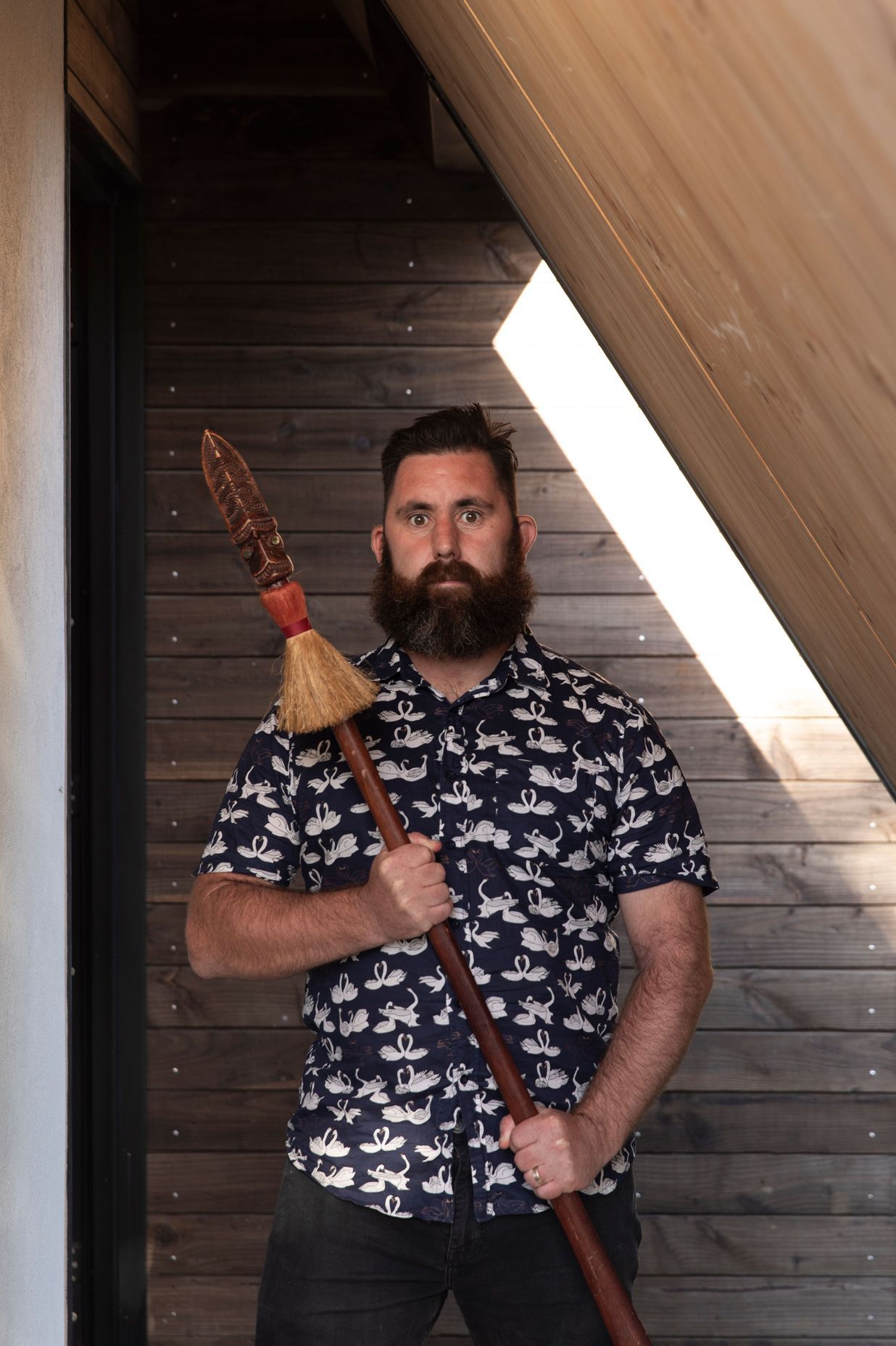 Designer Craig Wilson in the porch of his new home holding his taiaha.