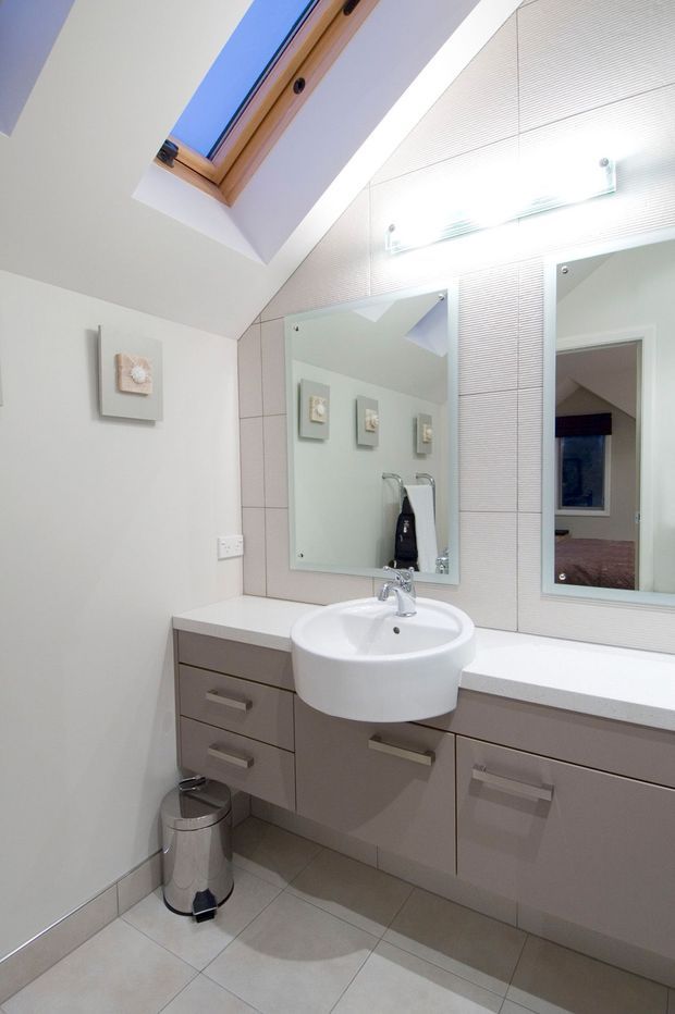 Bright, compact contemporary bathroom with a floating taupe vanity, white round basin, large mirrored wall cabinets, pale tiled floor, and a skylight set into the sloped ceiling. The mirror reflects an adjacent bedroom or hallway.