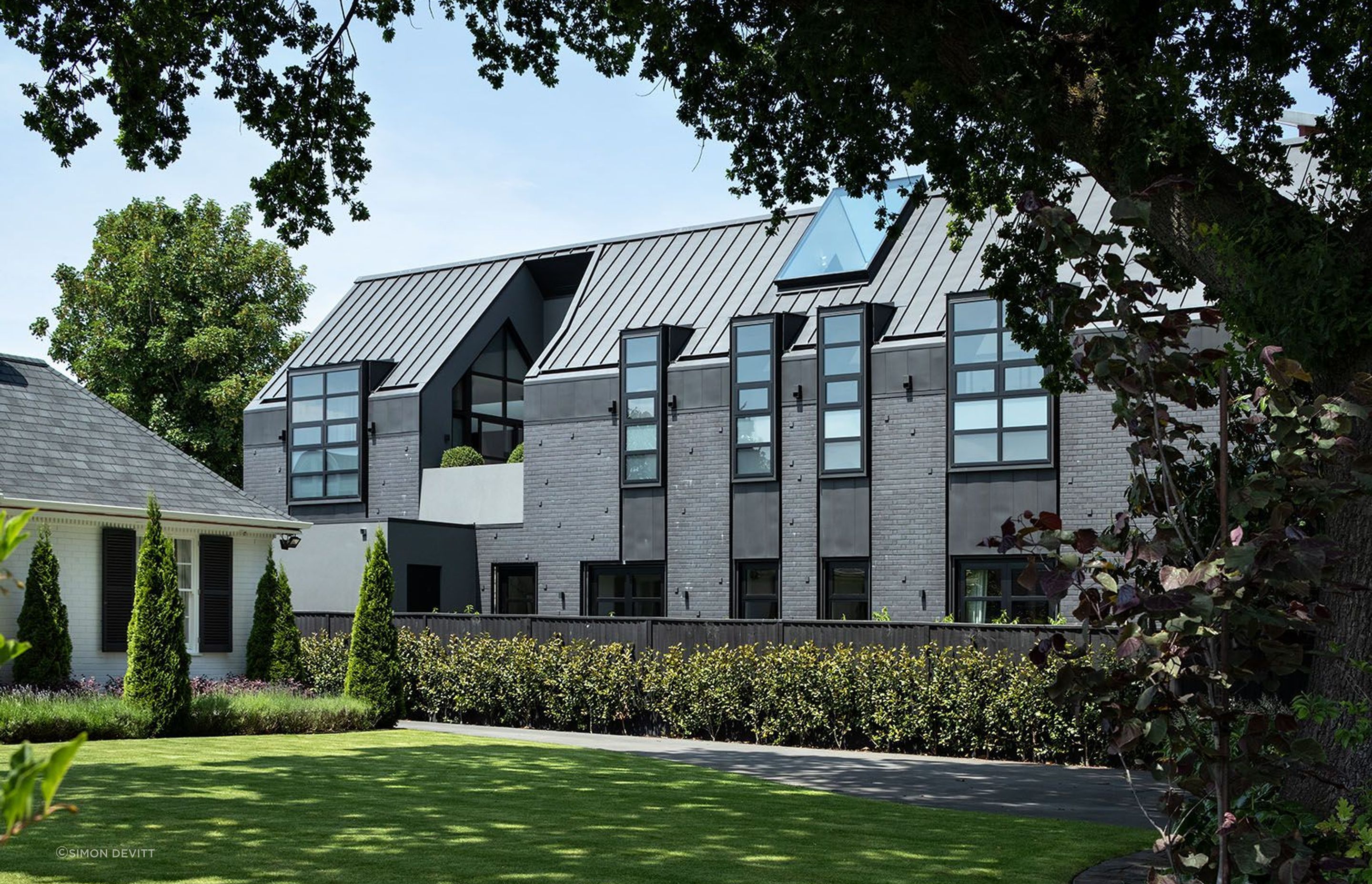 The Flemish bond brick façade combined with dormer windows and a patio carved out of the gabled form create a stunning and imposing elevation.