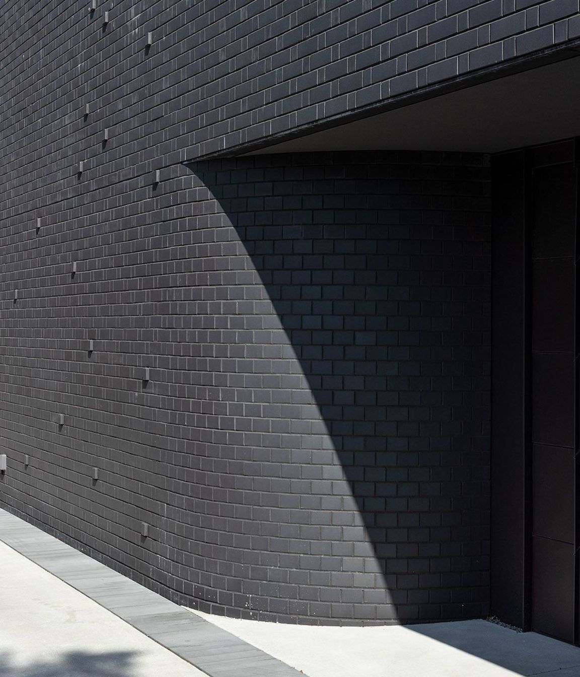 Introverted, the house reveals little to the outside while subtly creating intrigue. Its materiality and hue are drawn from loss, adding weight and silence to the form, that by day presents little to the passer by.