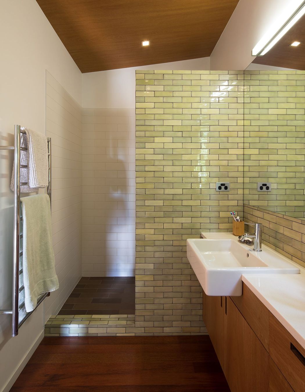 The shower is semi-enclosed behind an olive-green subway tiled wall.