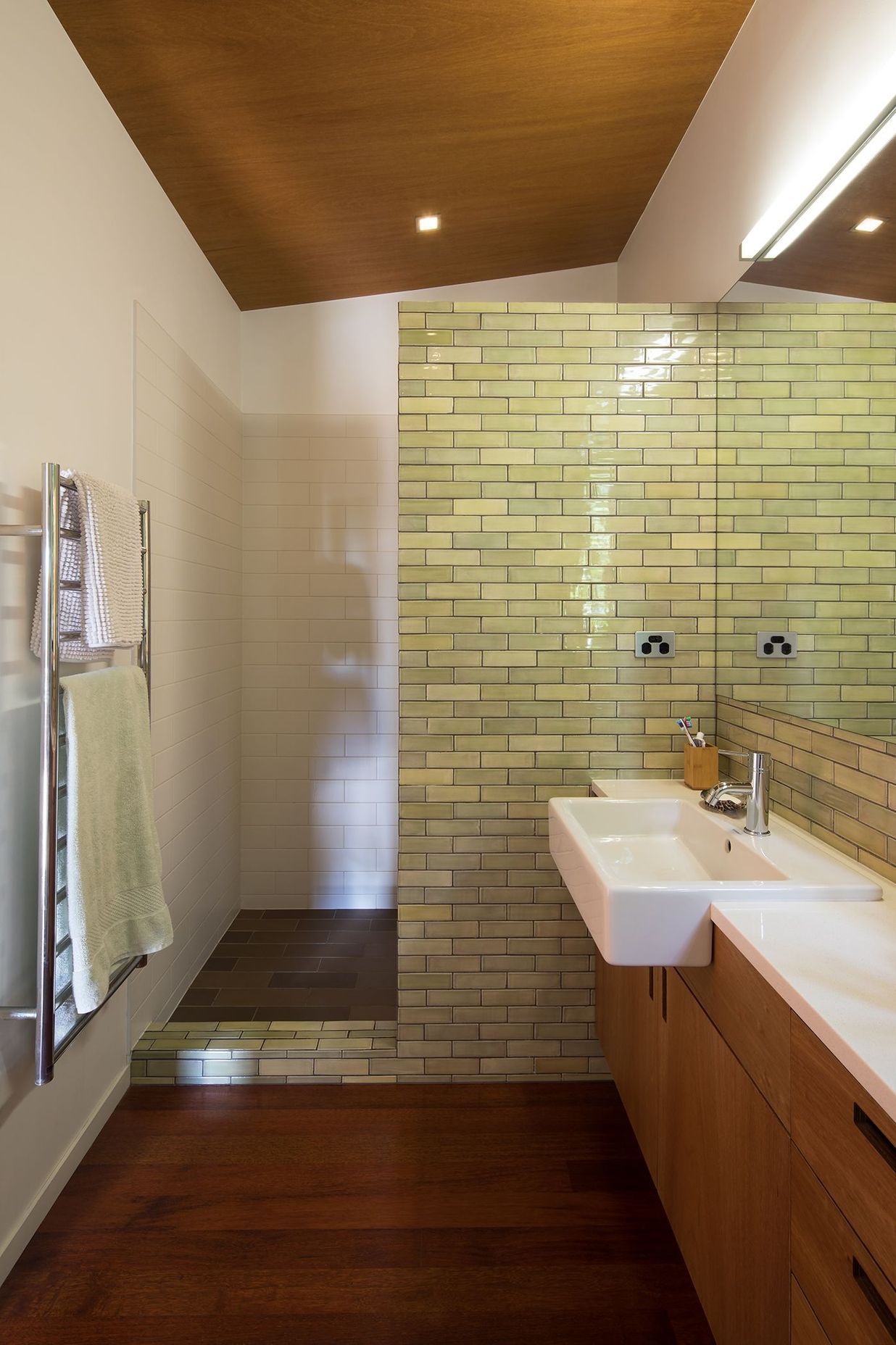 The shower is semi-enclosed behind an olive-green subway tiled wall.