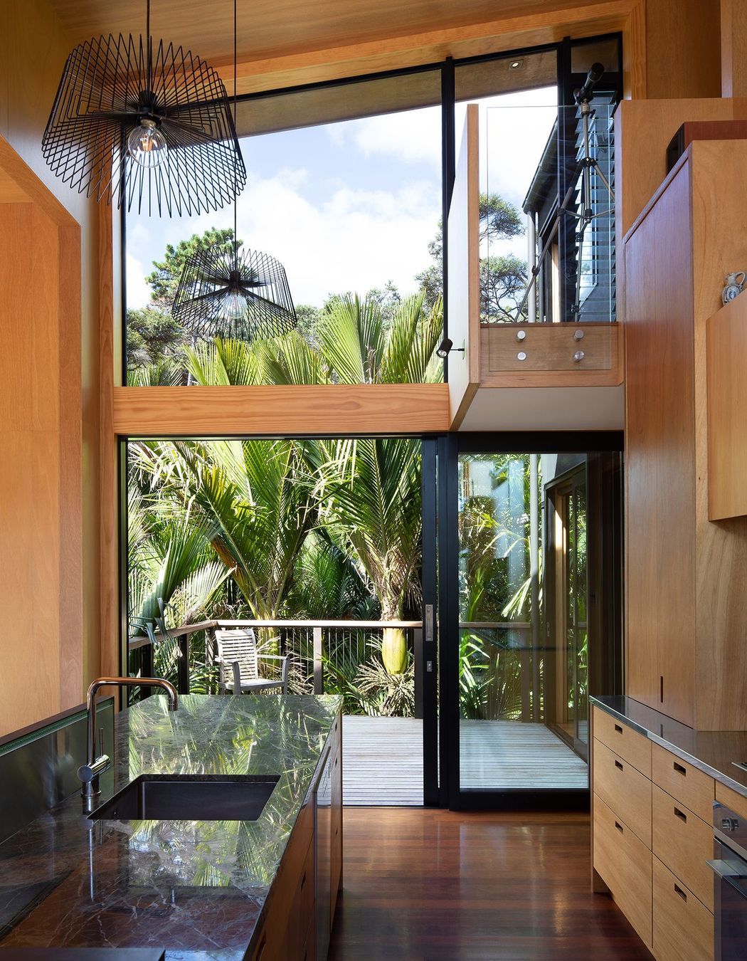 The kitchen opens straight out onto a deck and a cluster of nikau palms.