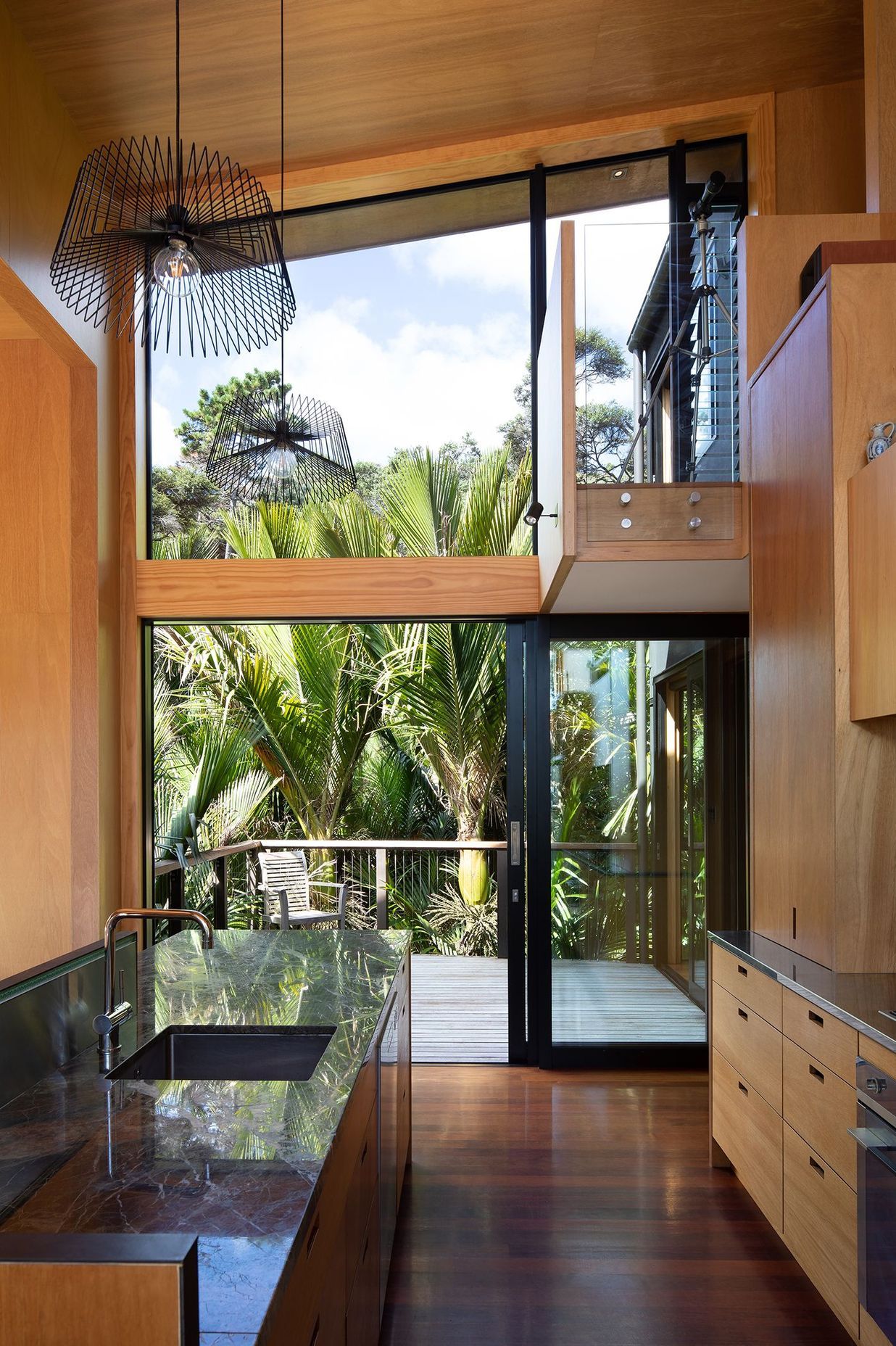 The kitchen opens straight out onto a deck and a cluster of nikau palms.
