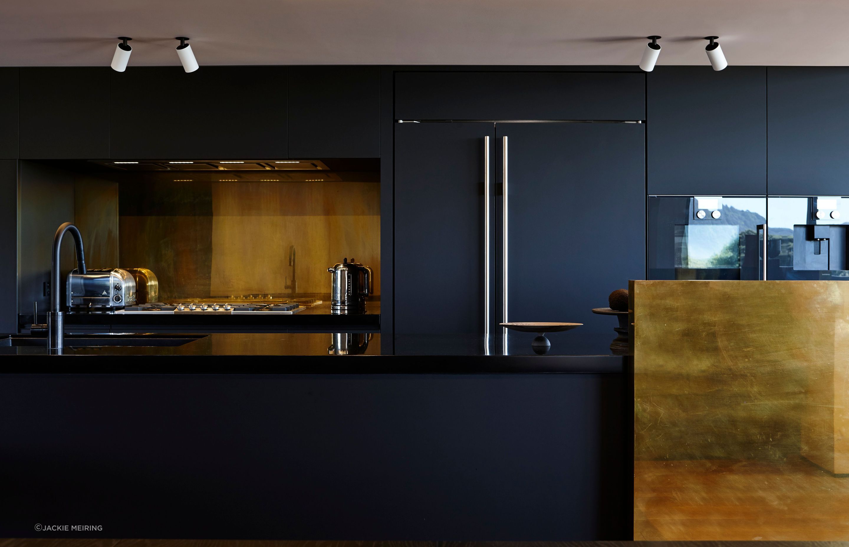 Copper elements accent the otherwise monochromatic kitchen, harnessing light and casting flashes of fire around the living room.
