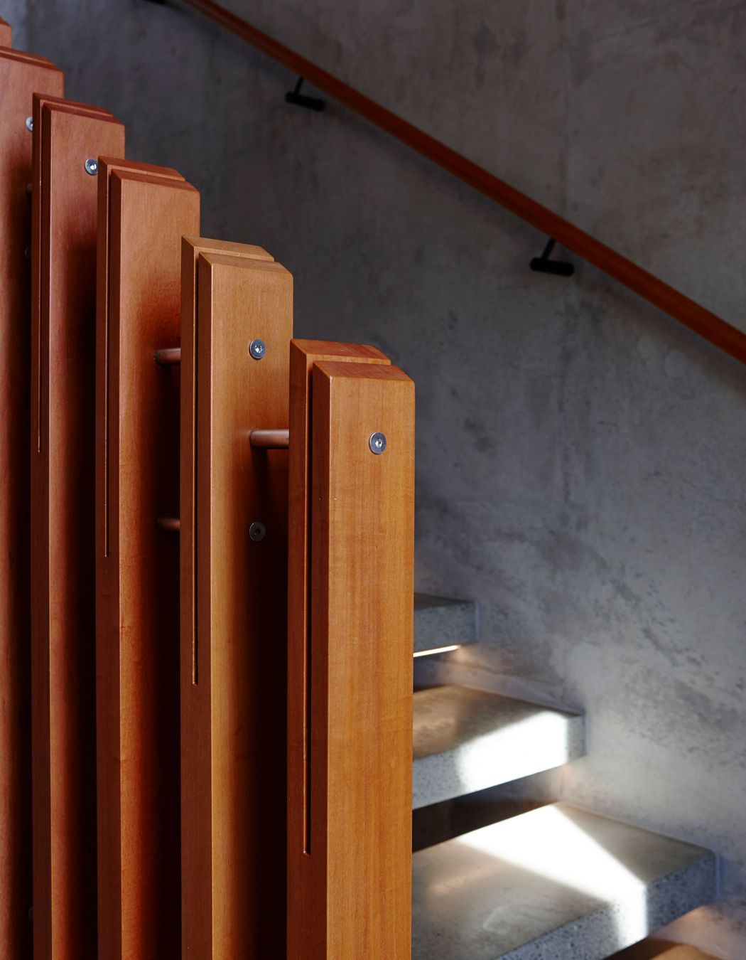 The richly toned timber handrail and ballusters impart a sense of warmth, juxtaposed against the cool concrete wall and treads.