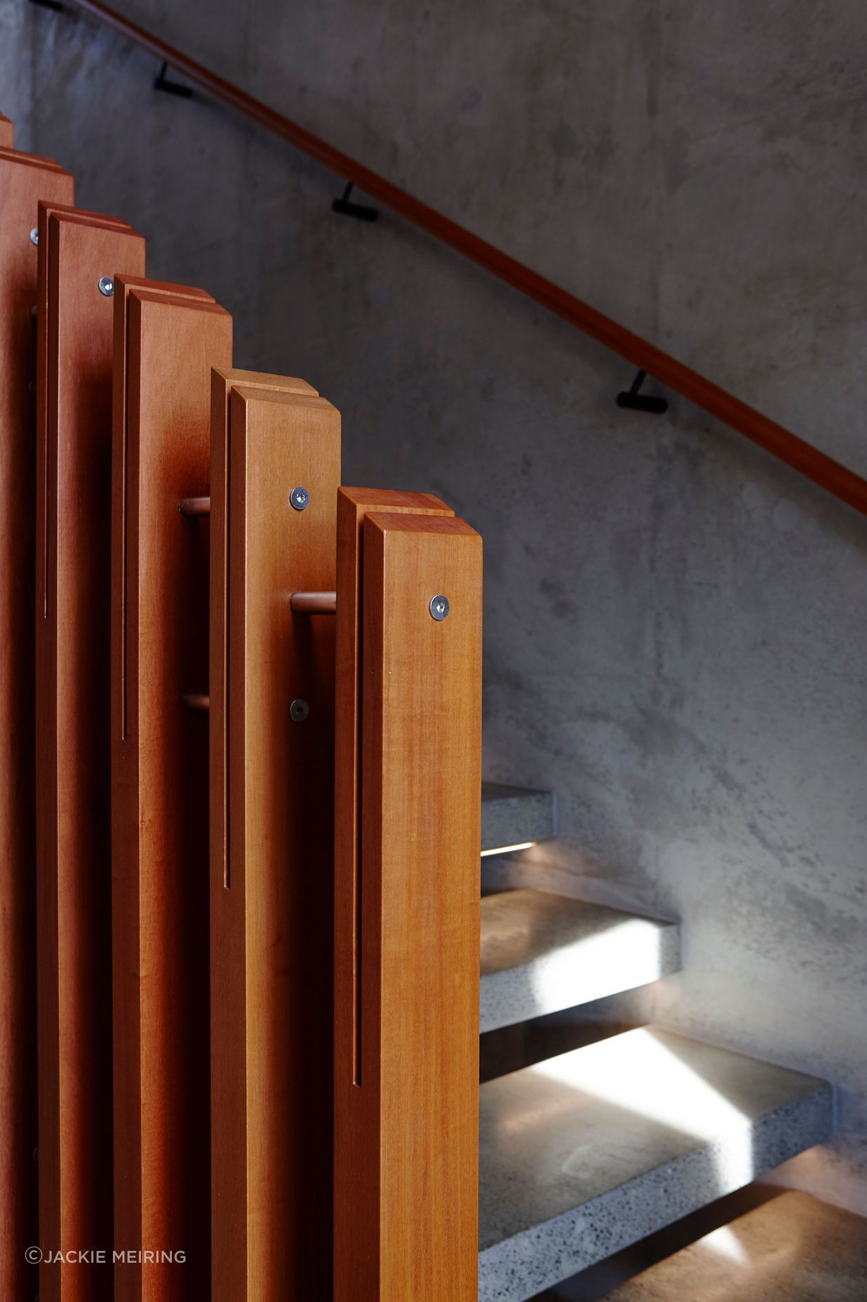 The richly toned timber handrail and ballusters impart a sense of warmth, juxtaposed against the cool concrete wall and treads.