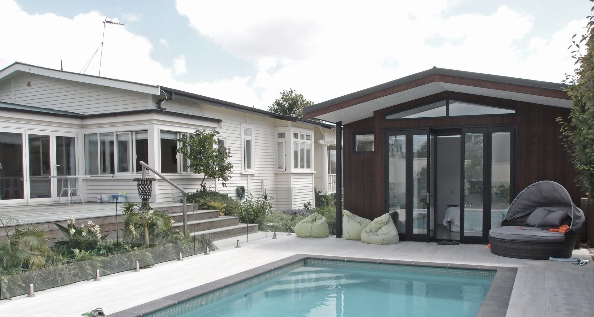 The new pool house faces the paved area and new subtropical planting beyond. Dark basalt edge coping contrasts with the marbled texture of the travertine tiles