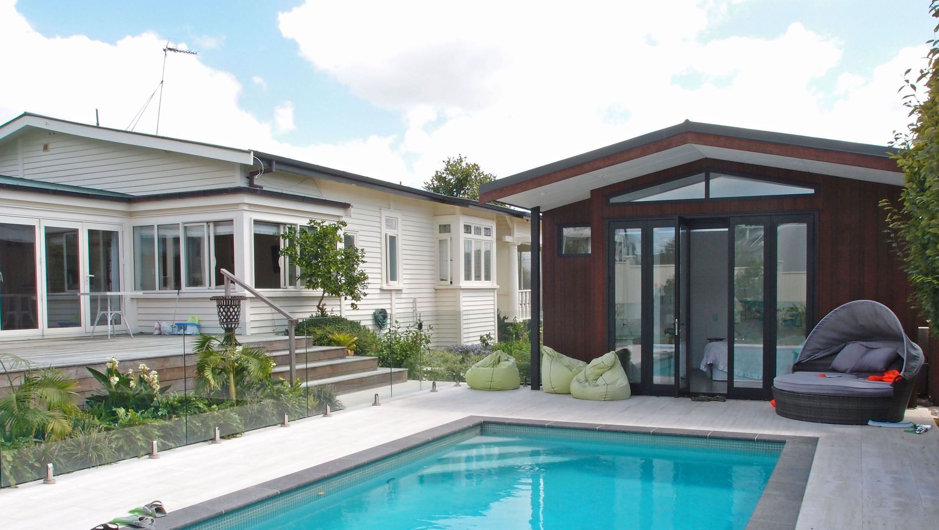 The new pool house faces the paved area and new subtropical planting beyond. Dark basalt edge coping contrasts with the marbled texture of the travertine tiles