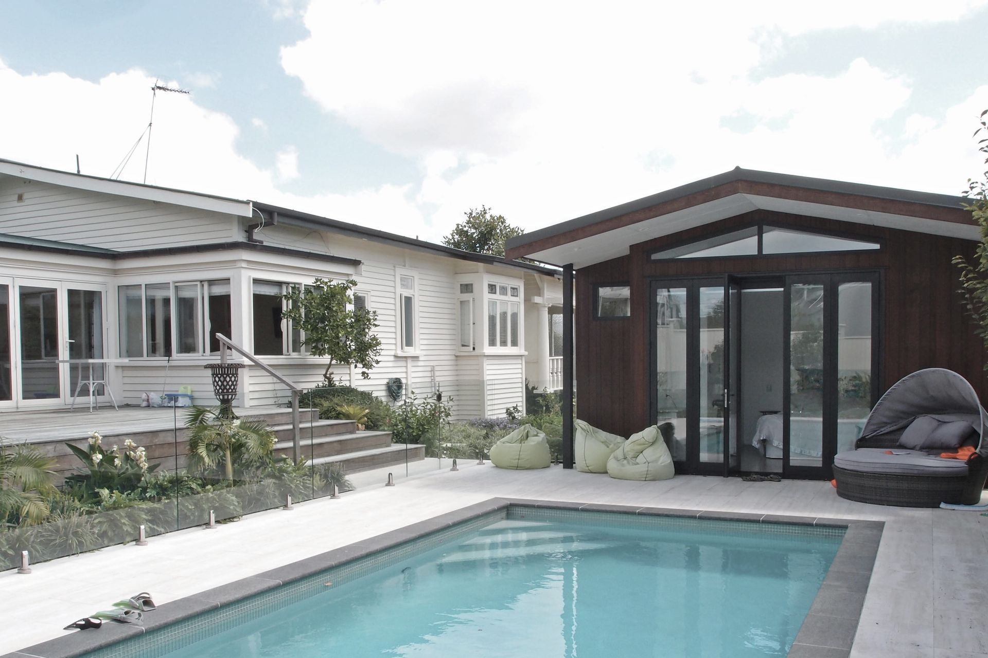 The new pool house faces the paved area and new subtropical planting beyond. Dark basalt edge coping contrasts with the marbled texture of the travertine tiles