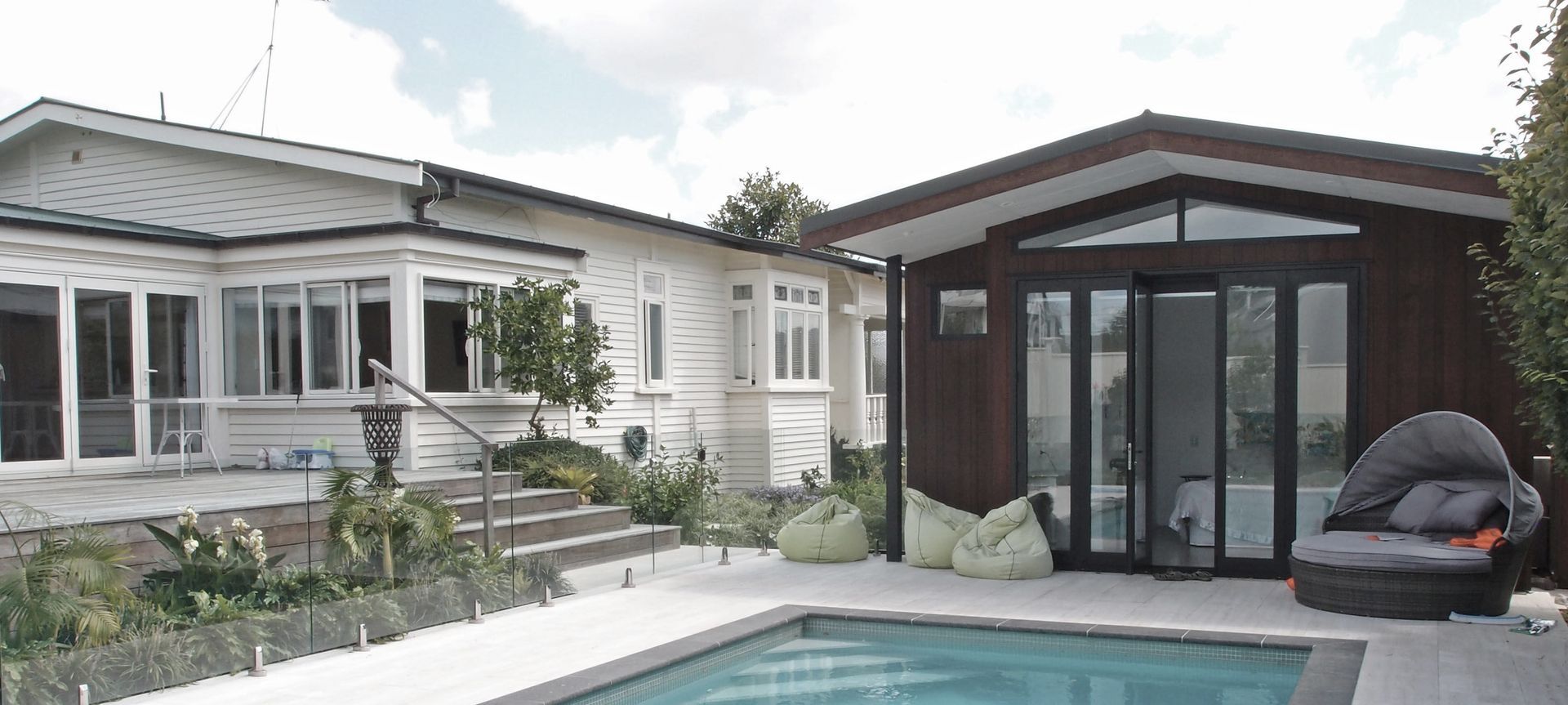 The new pool house faces the paved area and new subtropical planting beyond. Dark basalt edge coping contrasts with the marbled texture of the travertine tiles