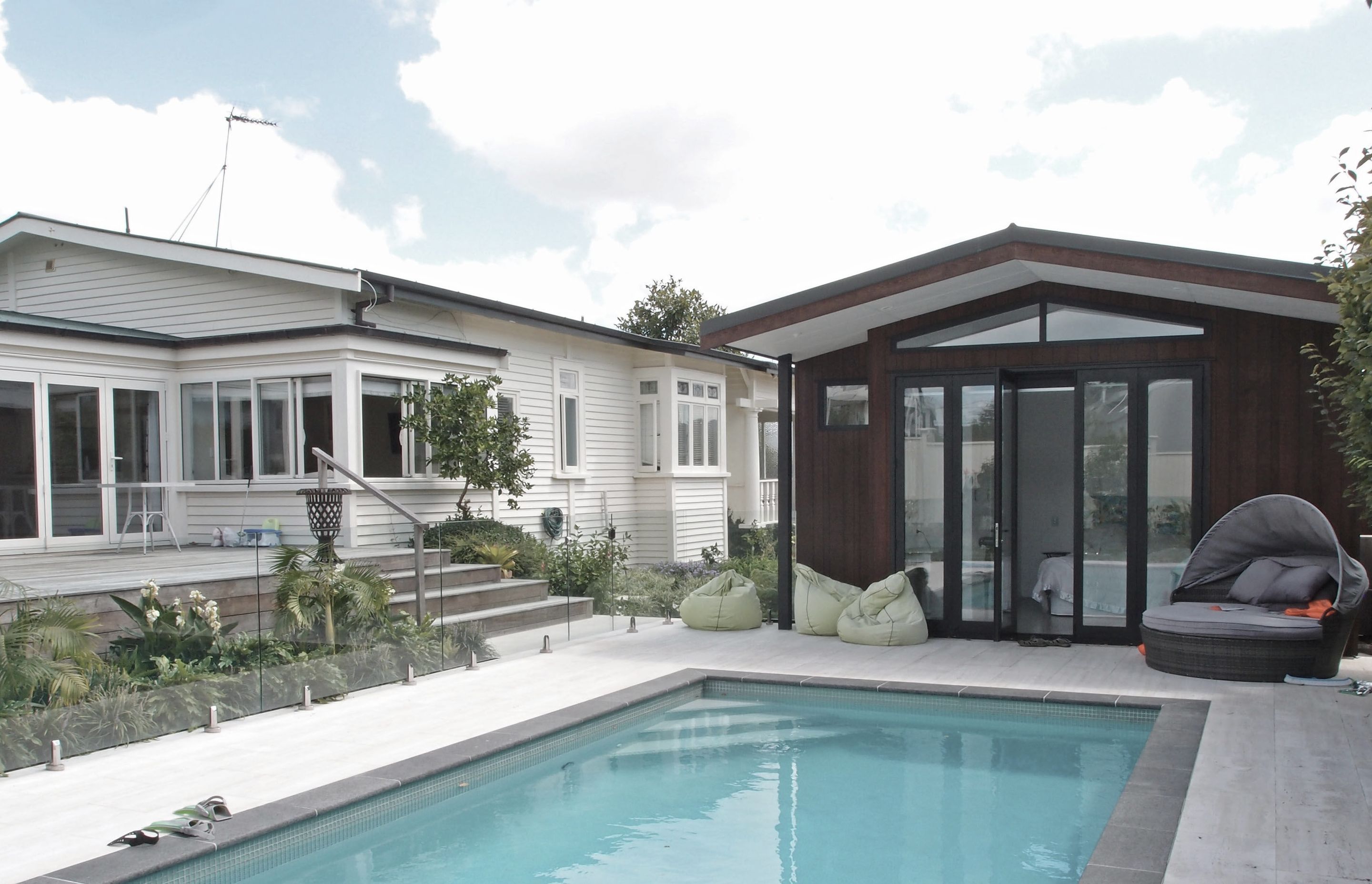 The new pool house faces the paved area and new subtropical planting beyond. Dark basalt edge coping contrasts with the marbled texture of the travertine tiles