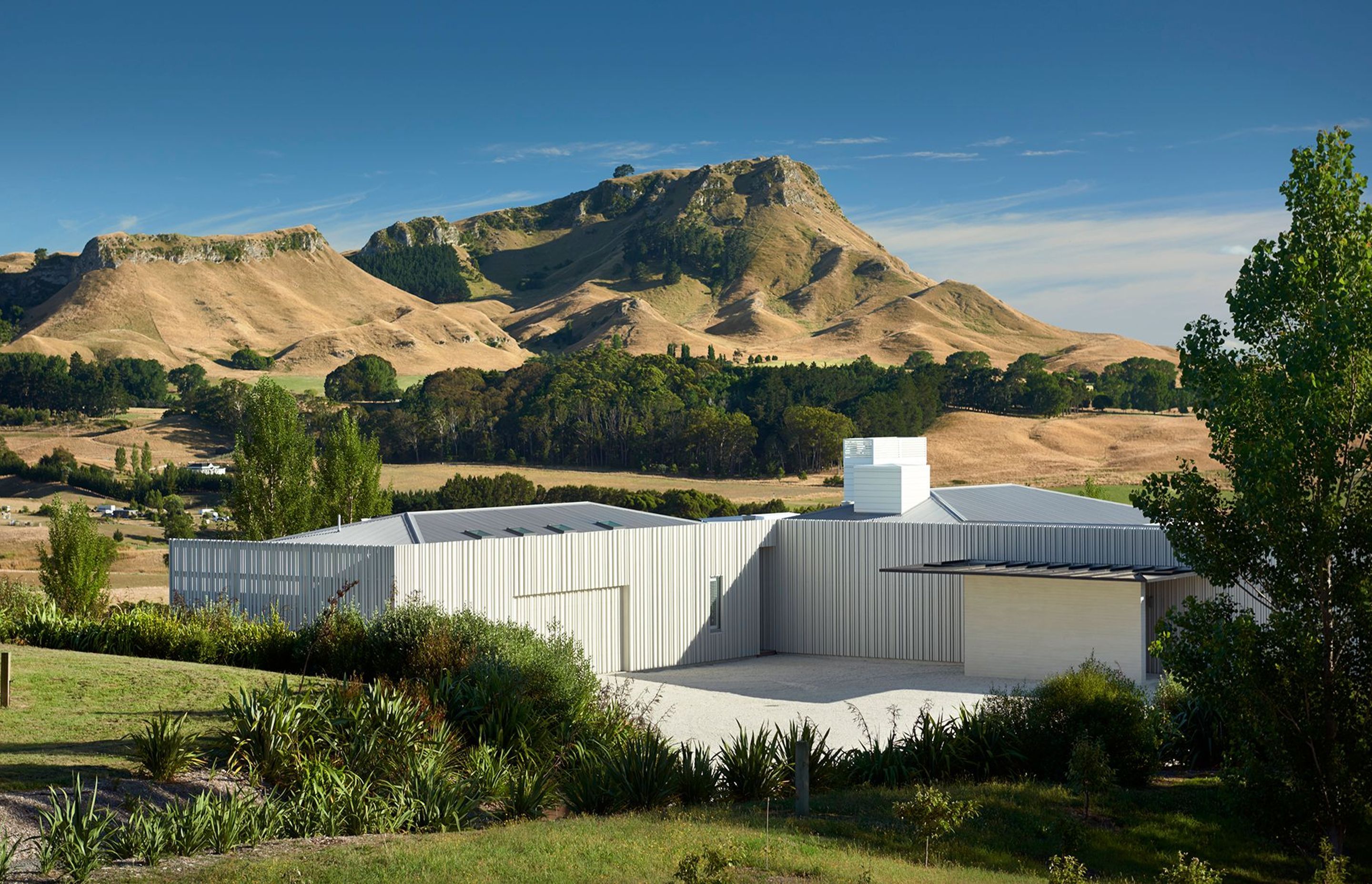 Hipped roofs peep up from the modern cladding, emulating the hilly topography of the surrounding landscaping with Te Mata Peak rising up in the distance.