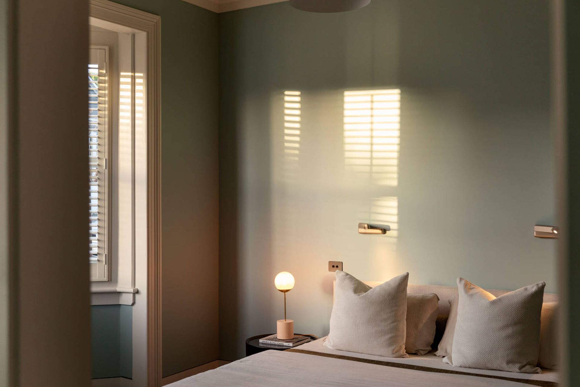 A master bedroom in the original villa features soft green walls that tie in with the exterior paint colour.