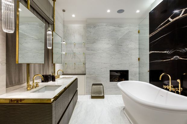 Luxurious contemporary bathroom featuring a freestanding white bathtub, double vanity with marble benchtop, large marble wall and floor surfaces, black marble feature wall, gold-toned tapware and trims, glass shower enclosure, illuminated mirrors, and pendant lighting.