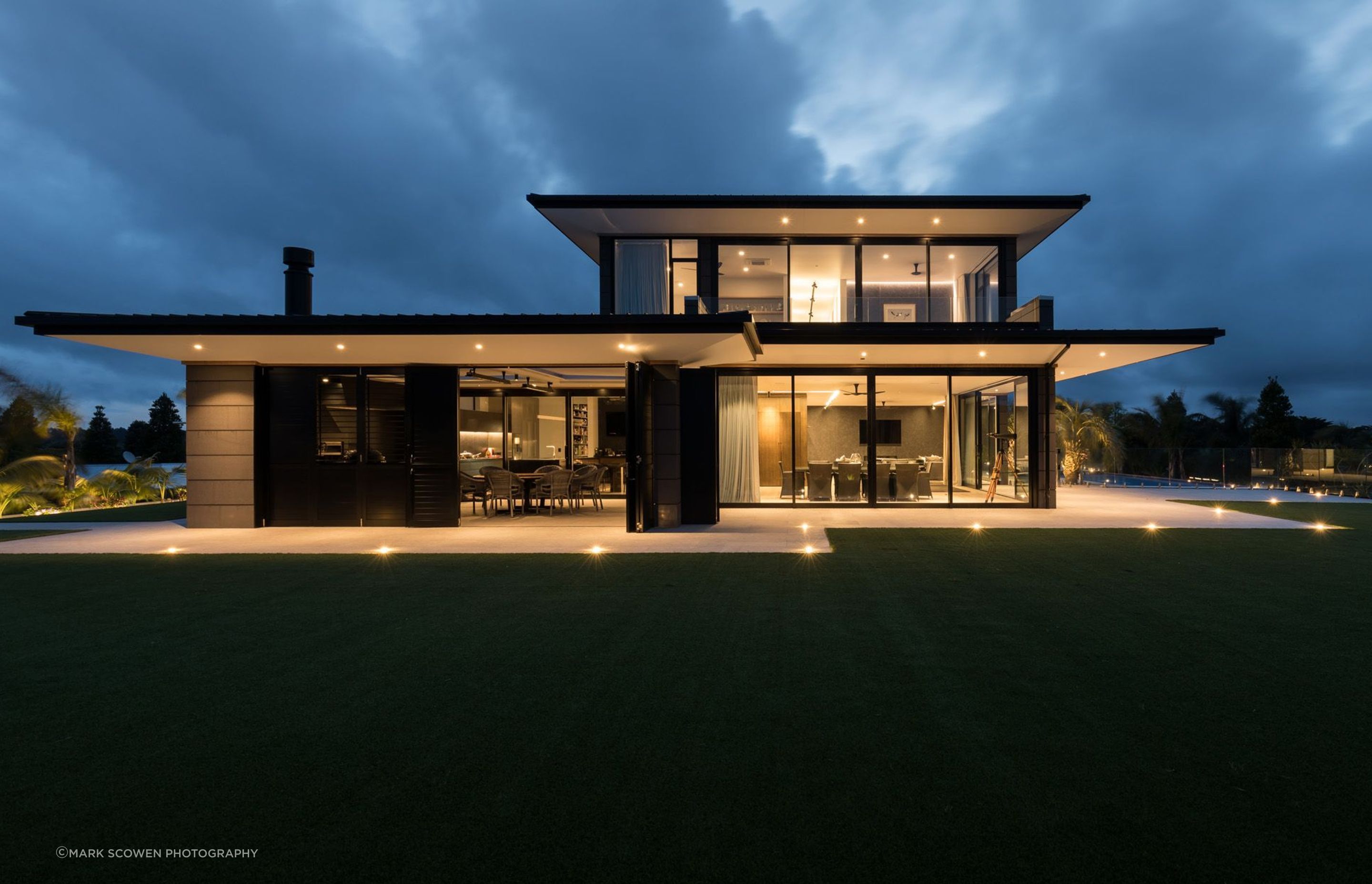 The eastern elevation lit up like a beacon at night, shows the outdoor room (left), the dining area (centre) and the swimming pool area (right).