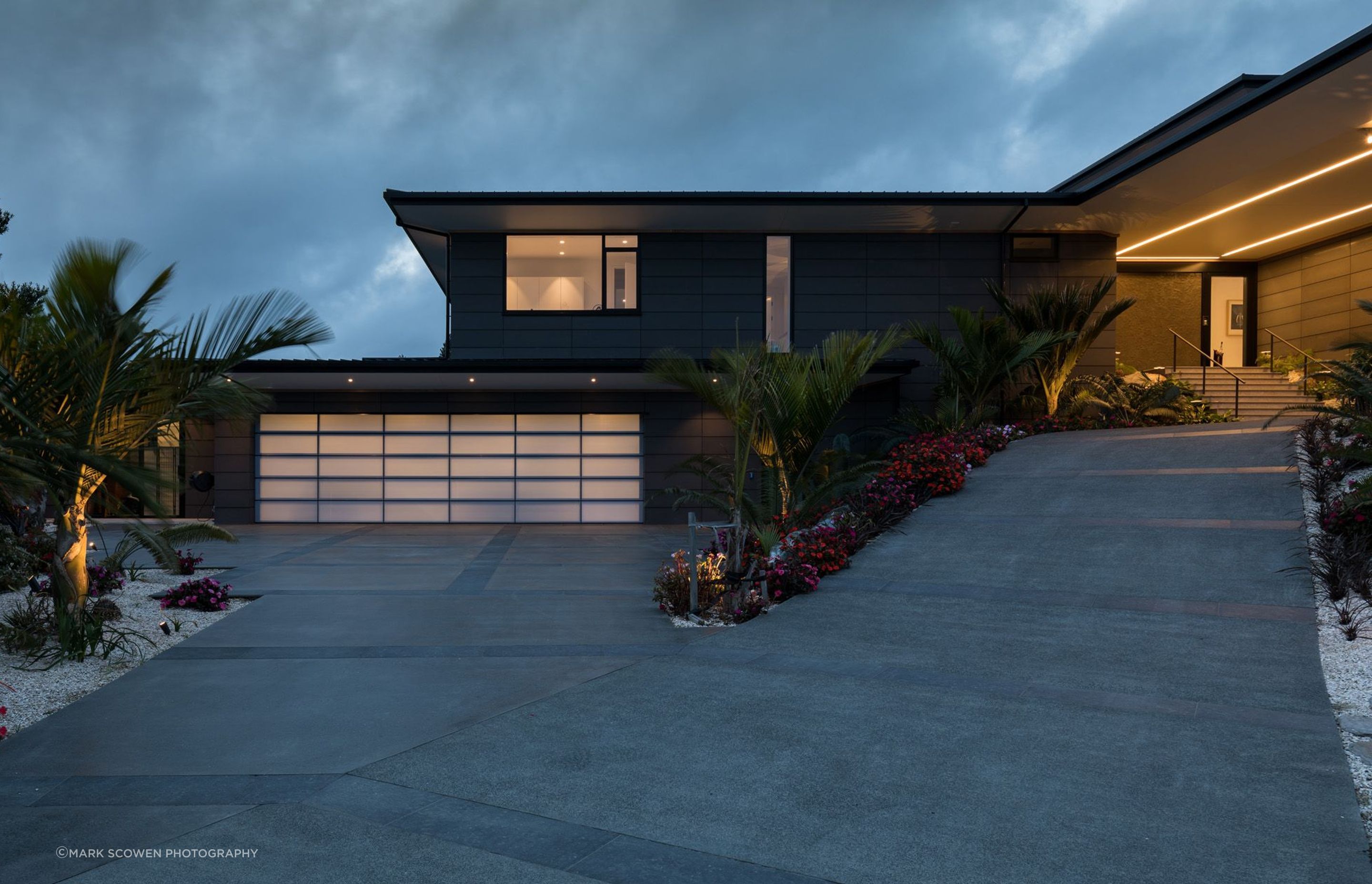 The front driveway leading the house is lined with sub-tropical plants. The garage (leftt) lights up like a lantern at night, while LED lights in the soffit direct visitors to the main entrance.