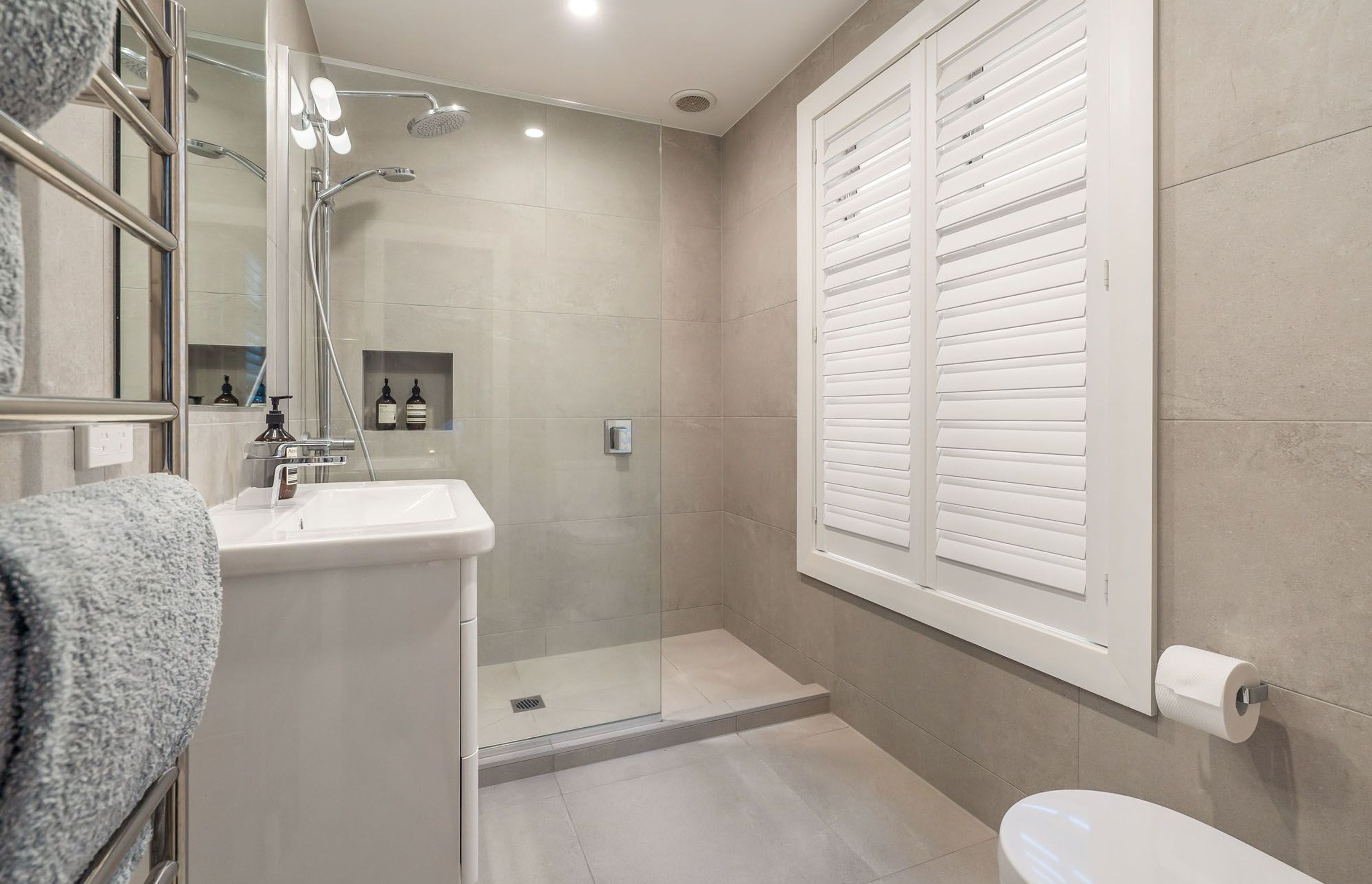 Similarly, this en suite bathroom has a very 'modern-classic' feel with traditional elements such as the shuttered window and Art Deco-style light fixture playing off against the modern fittings and colour scheme.