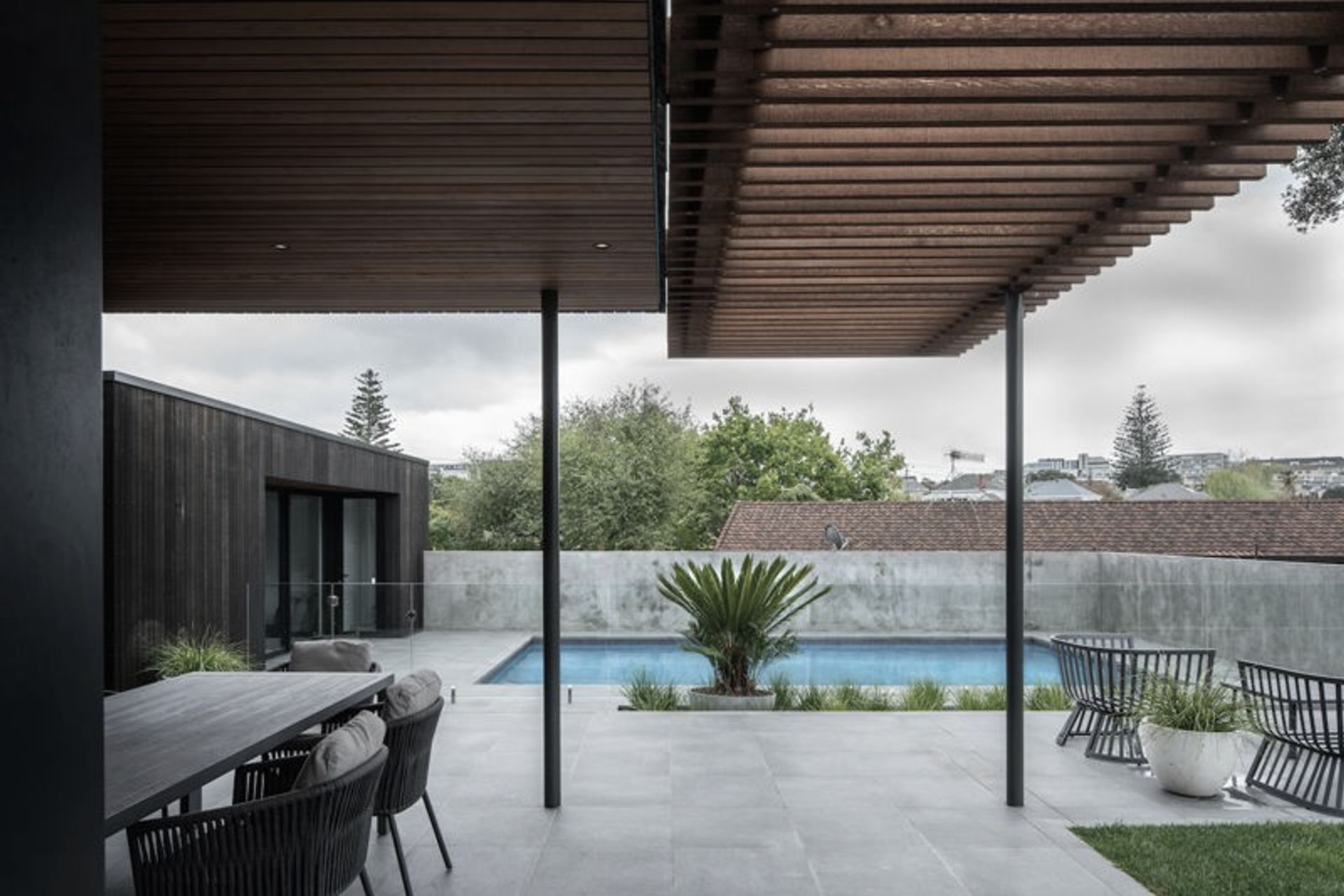 Combined, the interactionsof the new boxes with the original are contiguous and gracious as they converge around a Brutalist pool area flanked by concrete walls, glass fencing and textured grey tiles.
