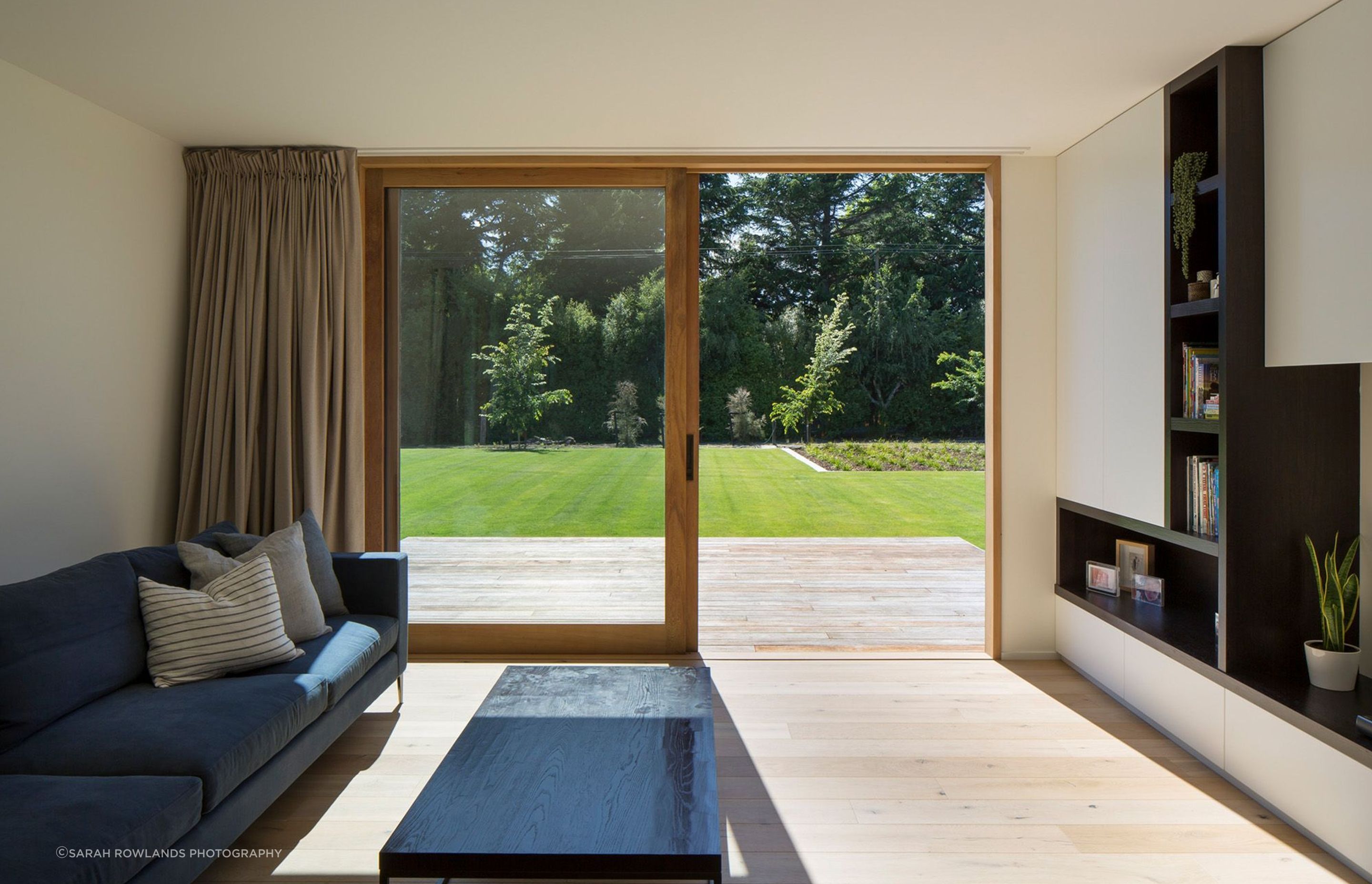 The other lounge area opens right up to a decked area and features custom-built shelving and an ink-coloured sectional sofa by Trenzseater.