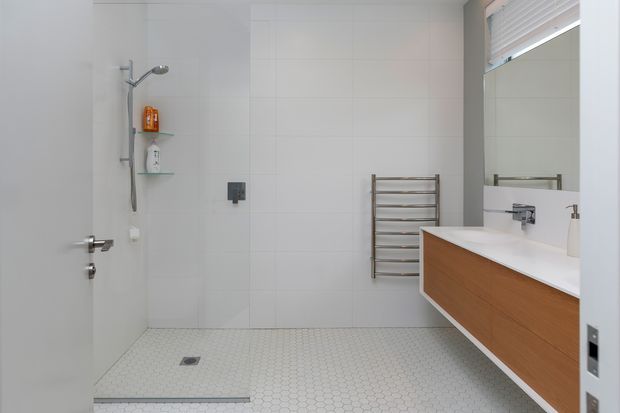 Bright contemporary bathroom with a walk-in tiled shower, white hexagonal floor tiles, large light wall tiles, a wall-mounted timber vanity with white countertop, mirrored cabinet, chrome tapware, and a heated towel rail.