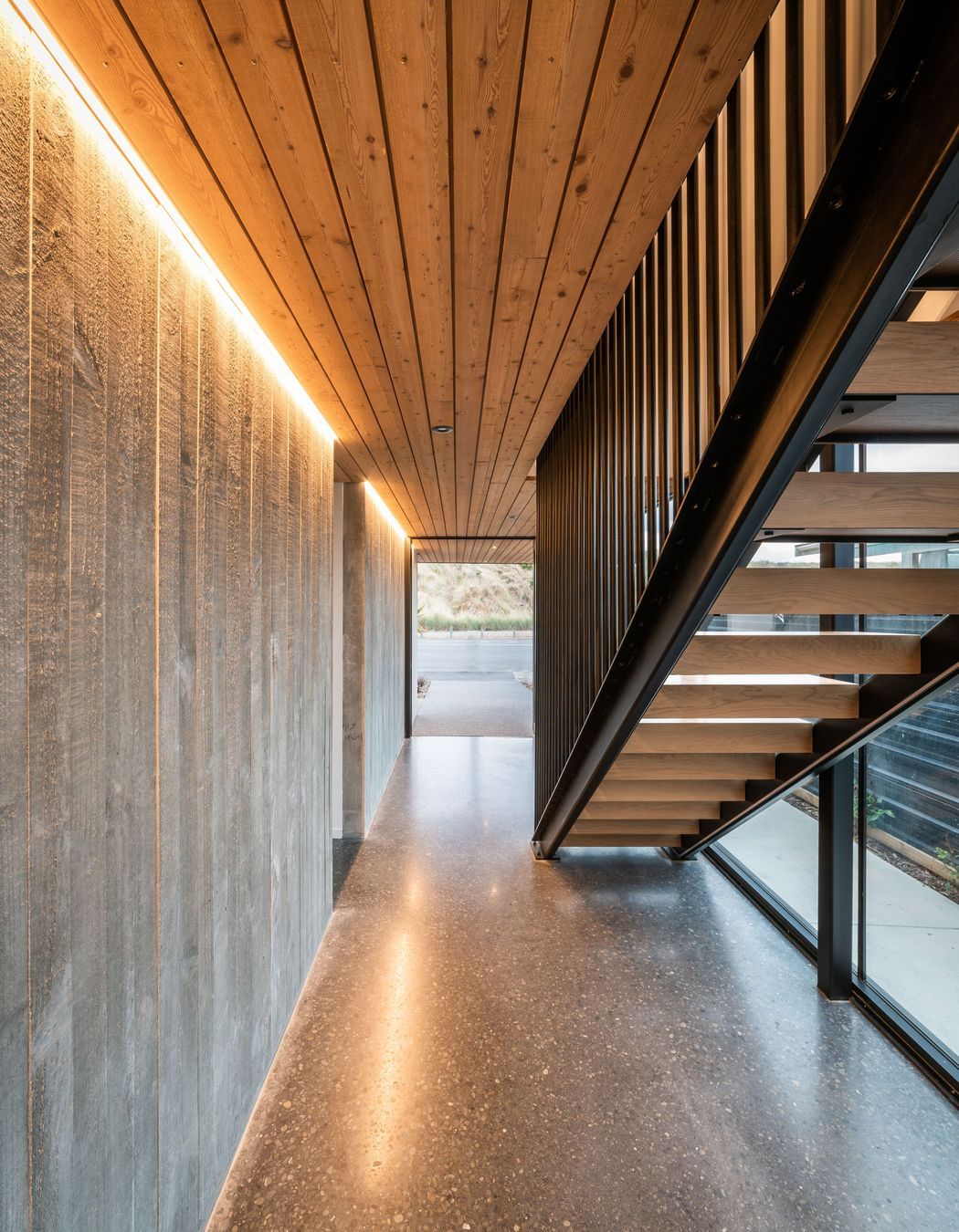 A board form concrete wall, larch ceiling and and black steel balustrades define the lower hallway