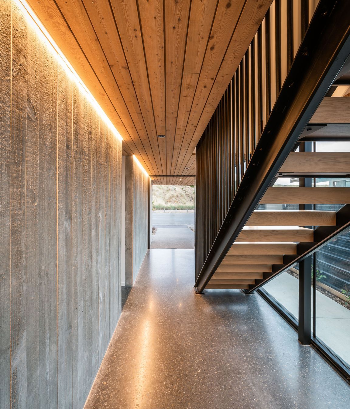 A board form concrete wall, larch ceiling and and black steel balustrades define the lower hallway 